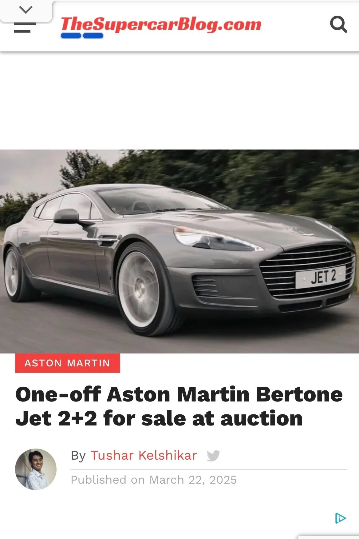 A silver Aston Martin Bertone Jet 2+2 car driving on a road, with a blurred background of trees, featured on TheSupercarBlog.com with article title about a one-off model for sale at auction.