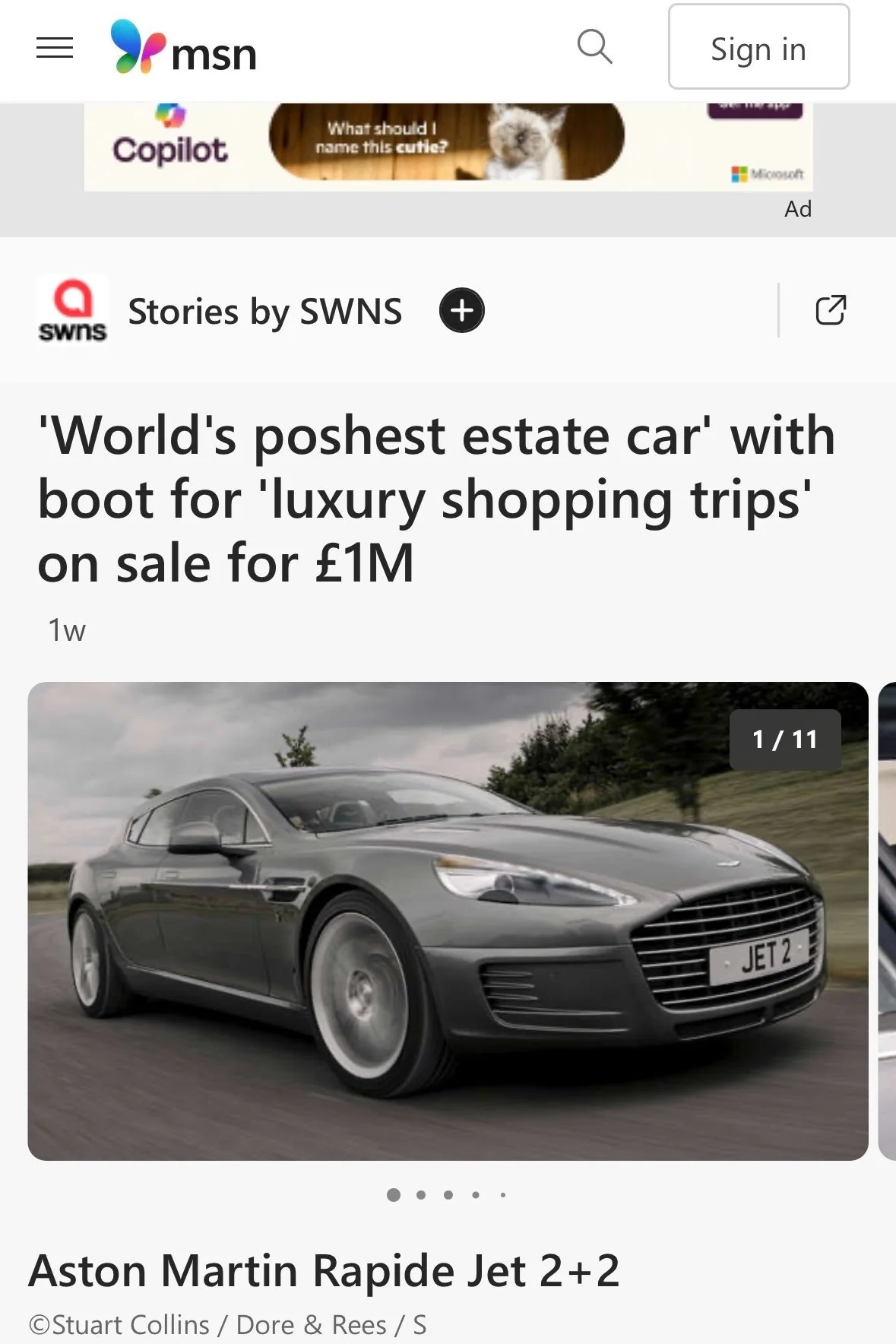 A gray Aston Martin Rapide Jet 2+2 car driving on a road with trees and a cloudy sky in the background.