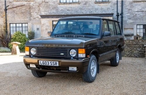 Black classic Range Rover parked outdoors in front of a stone building with windows and greenery.