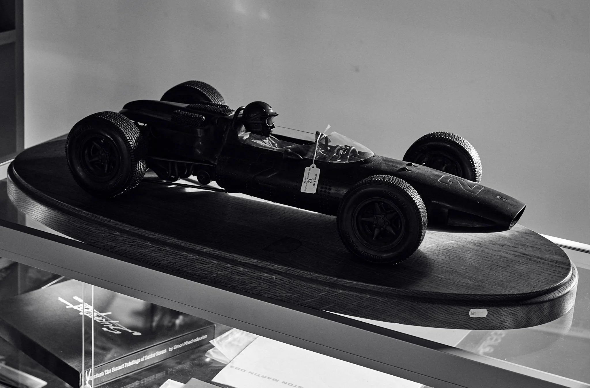 A black and white model of a vintage racing car displayed on a wooden base in a glass case.