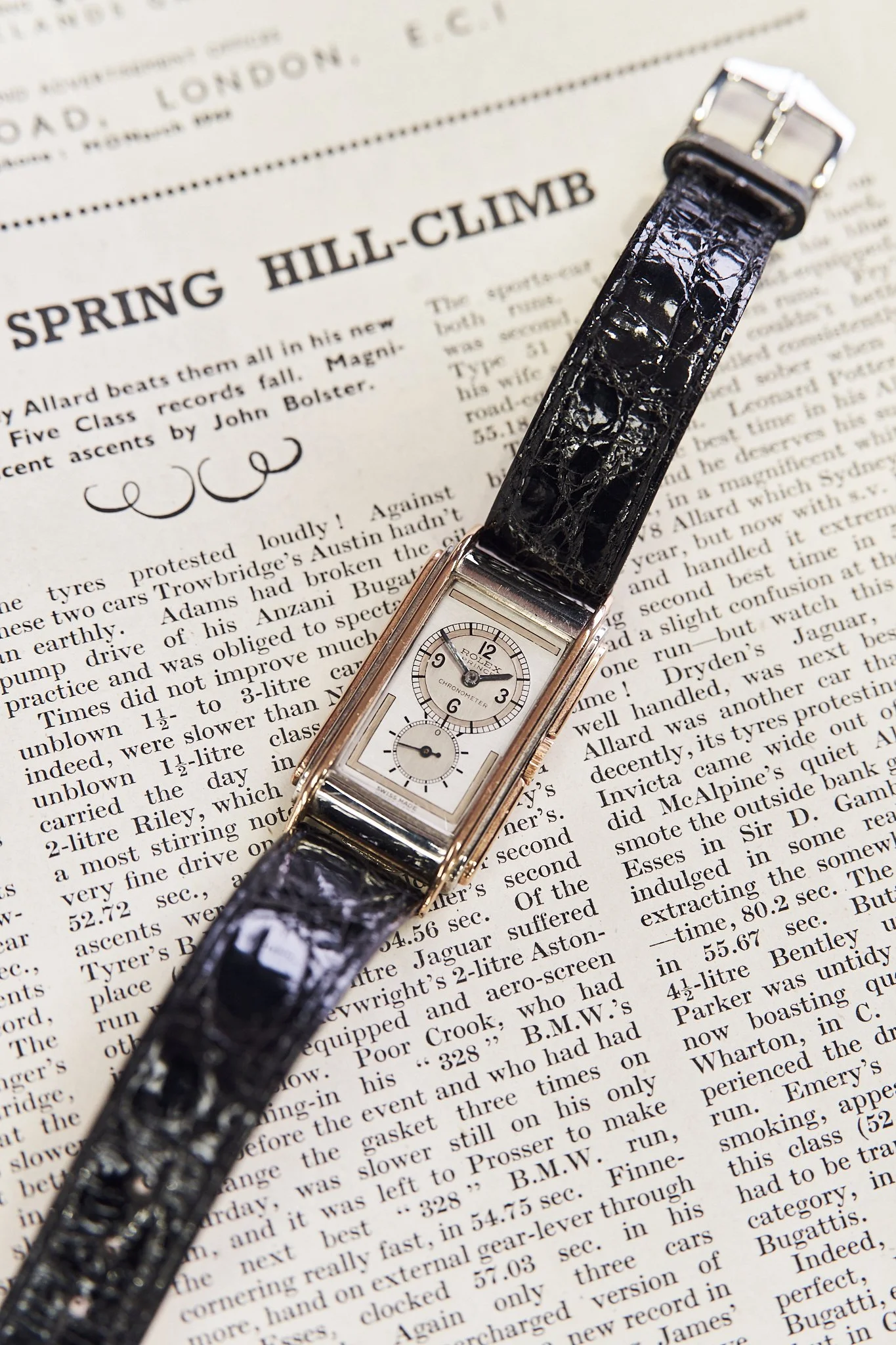 A watch with a black leather strap and two dials, placed on a newspaper.