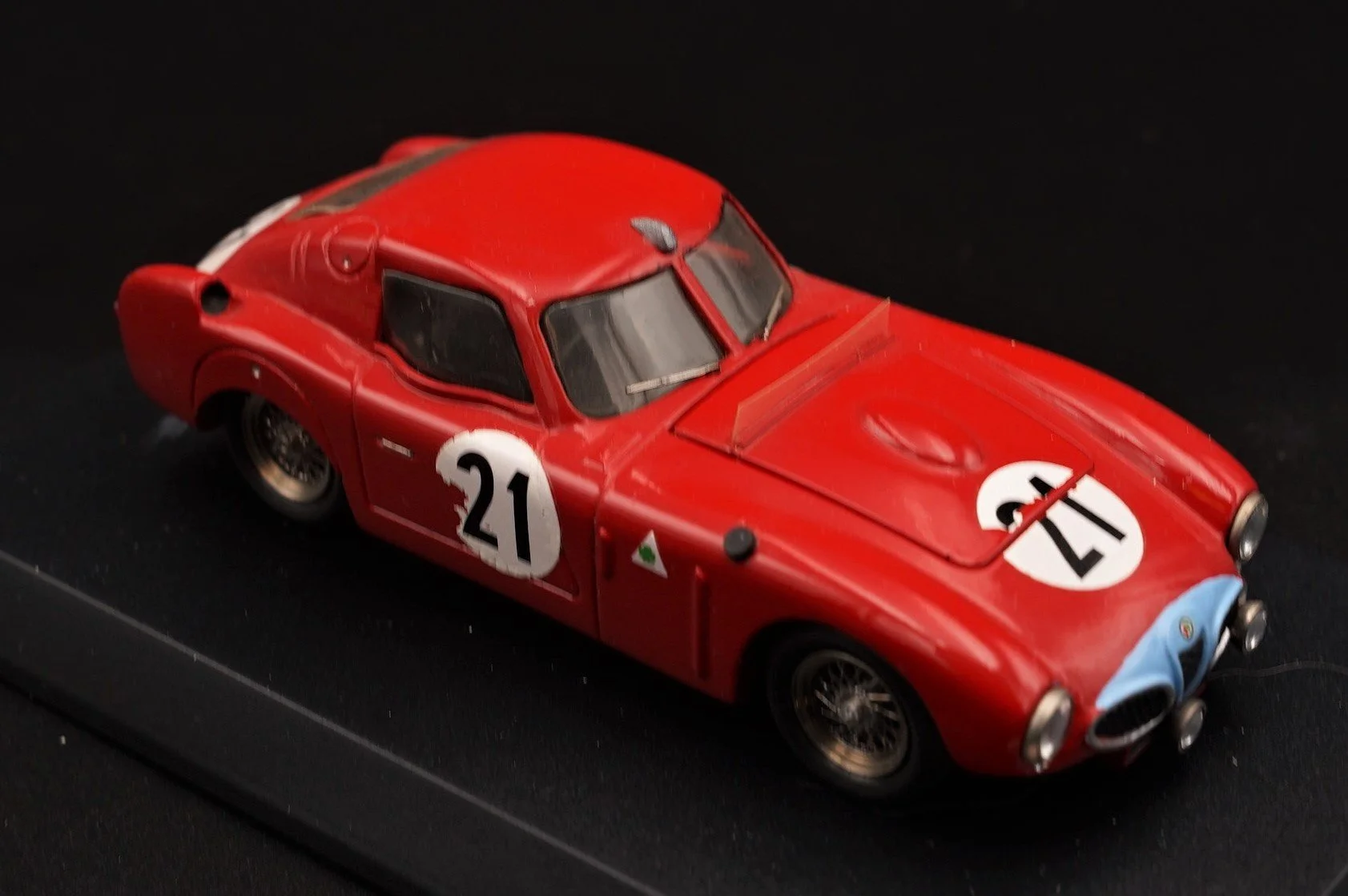 Red vintage racing car with the number 21 on the hood and side, black tires, black windshield, and Italy flag detail, displayed on a black surface.