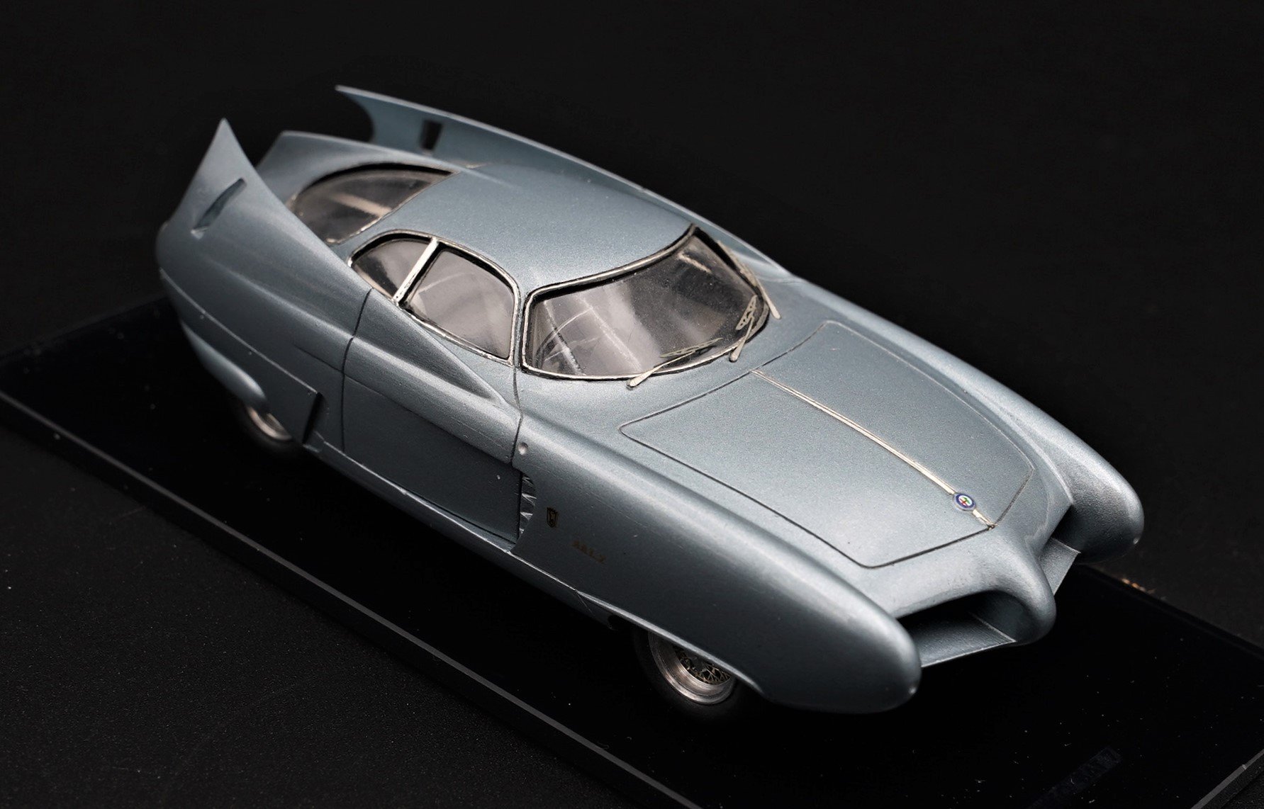 A detailed model of a vintage silver racing car on a black display base.