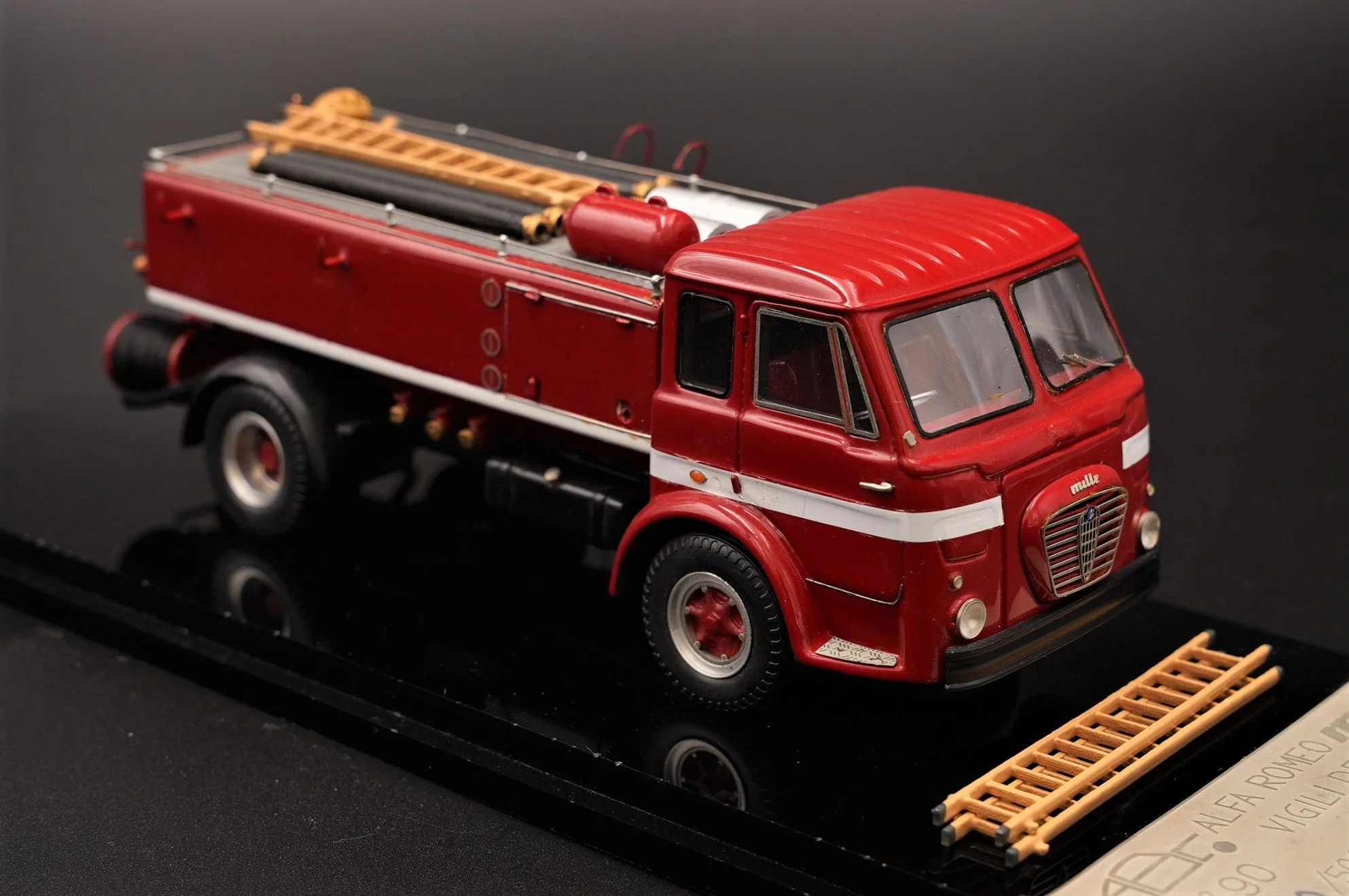Miniature red fire truck model with ladders and equipment on a display stand.