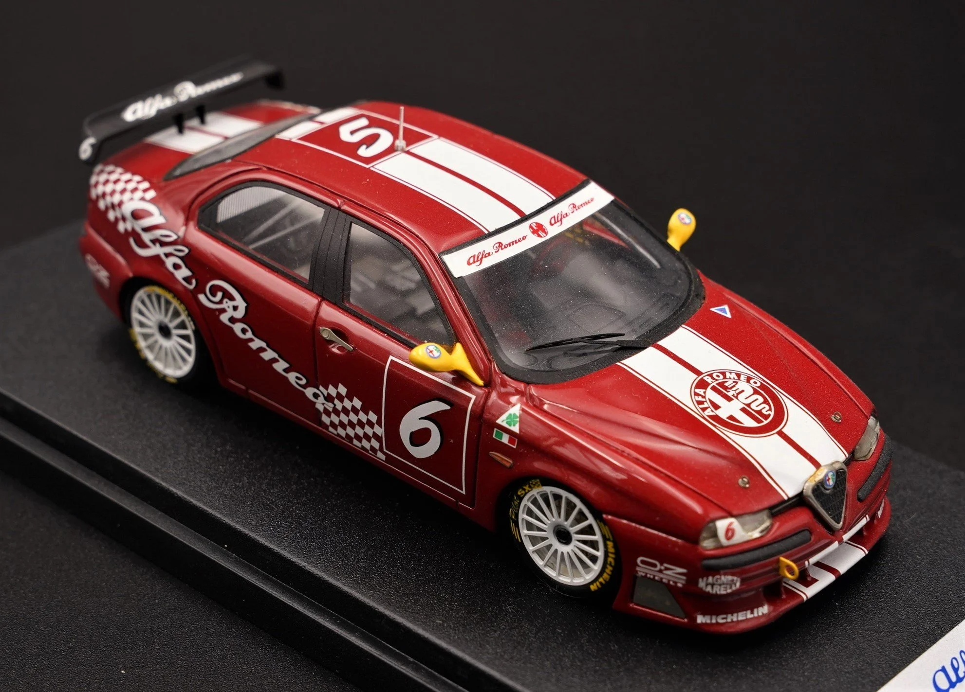 A detailed scale model of a red Alfa Romeo race car with white racing stripes and number 6, displayed on a black base.