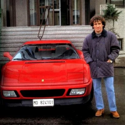 A man stands next to a red sports car, with a building and steps in the background.