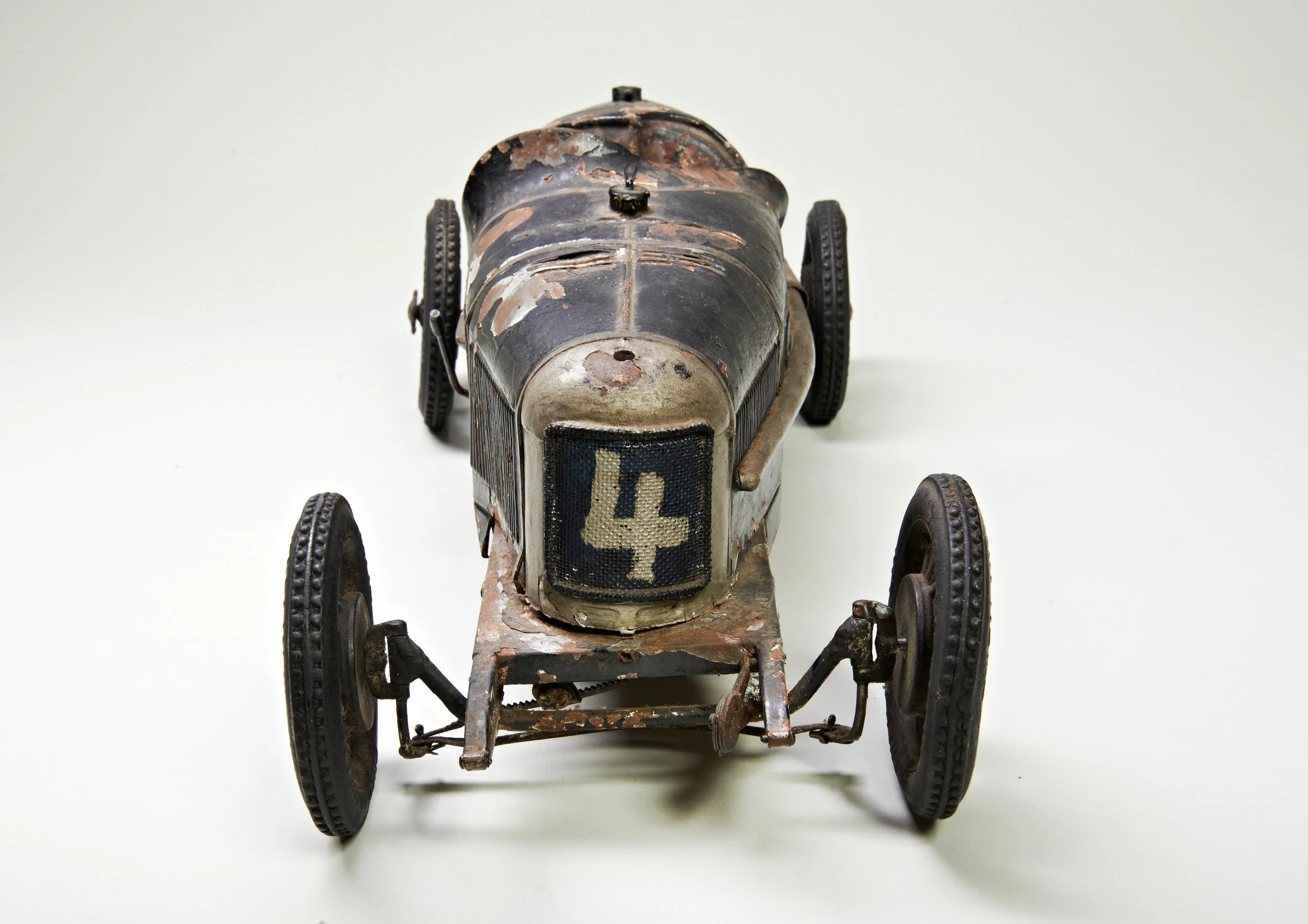 An old, rusty vintage racing car model with the number 4 on its front, placed on a plain white surface.