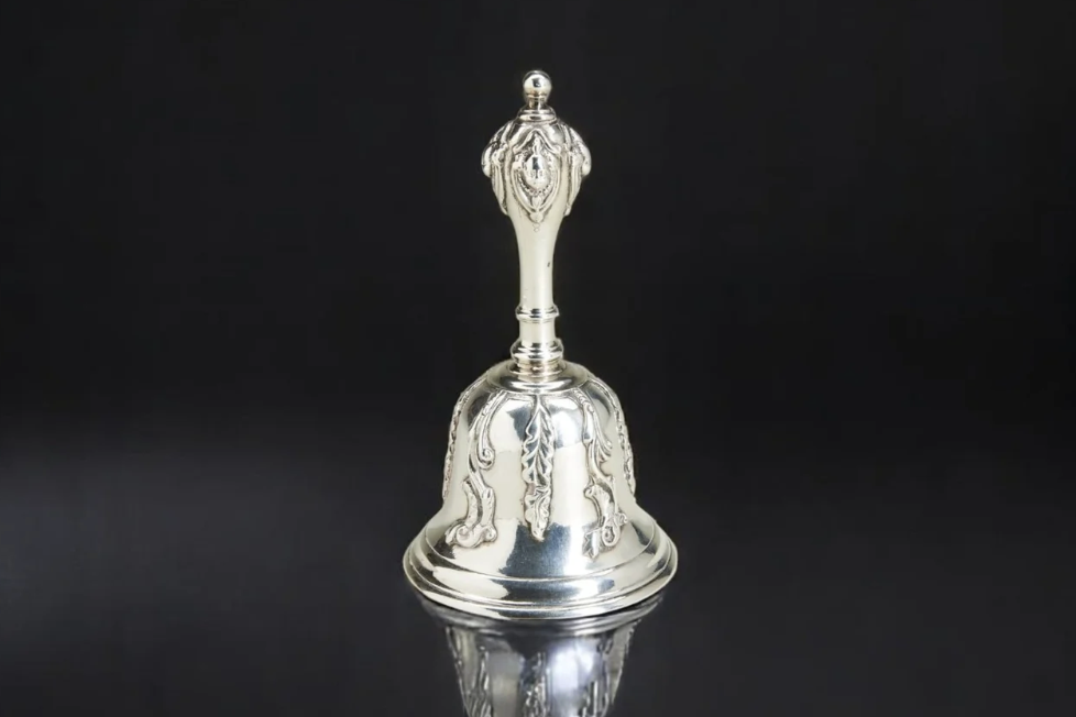 Silver decorative bell with intricate engravings on a black background.