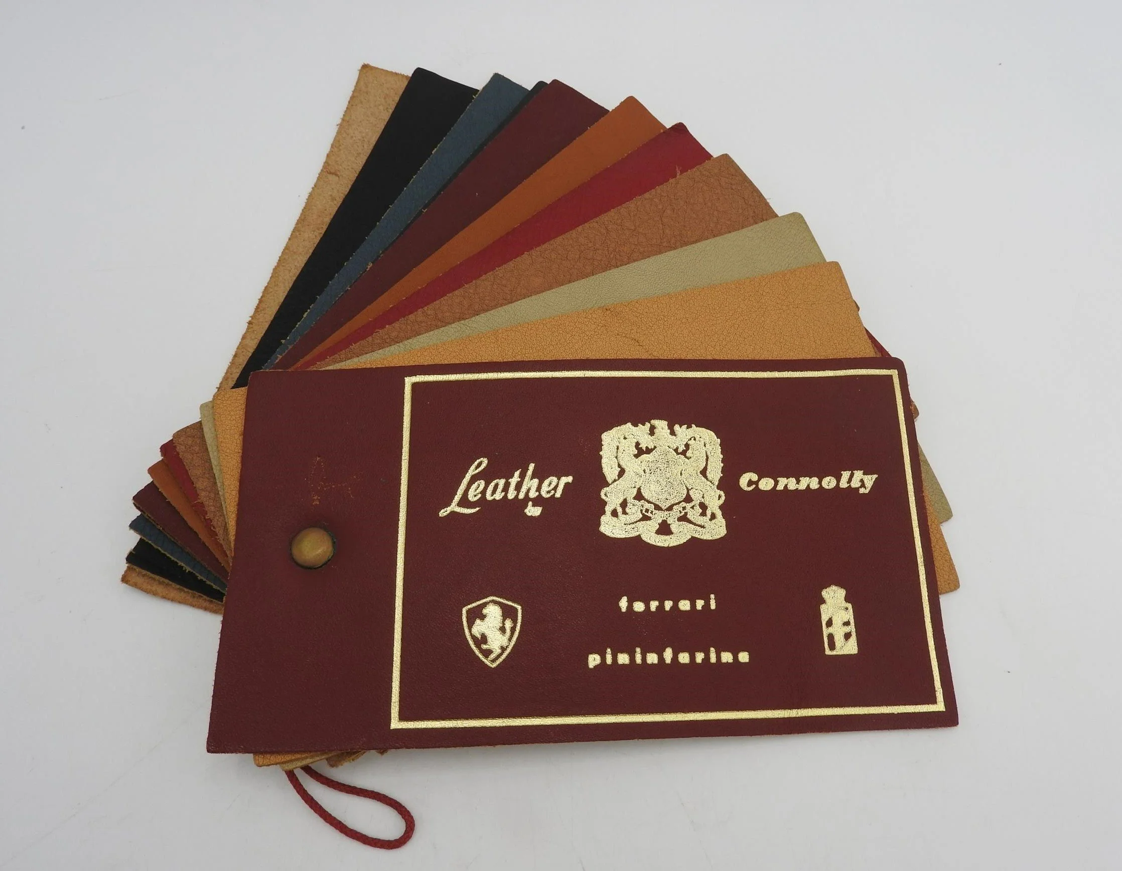 A sample booklet of various faux leather color swatches fanned out, with a burgundy cover labeled "Leather Connelly" including a lion emblem, a small shield icon, and a leather bottle icon.