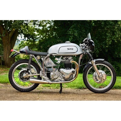 Classic silver motorcycle parked outdoors on a dirt path with green trees in the background.