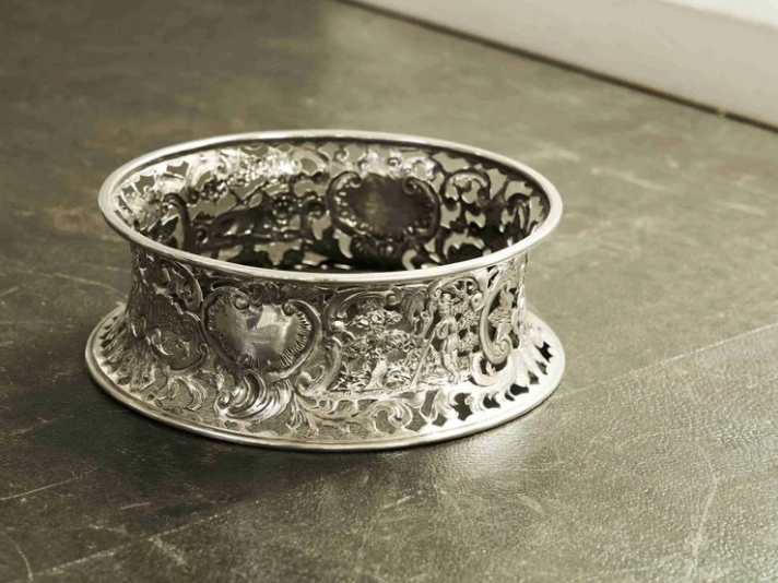 A silver decorative bracelet with intricate cut-out patterns resting on a dark surface.