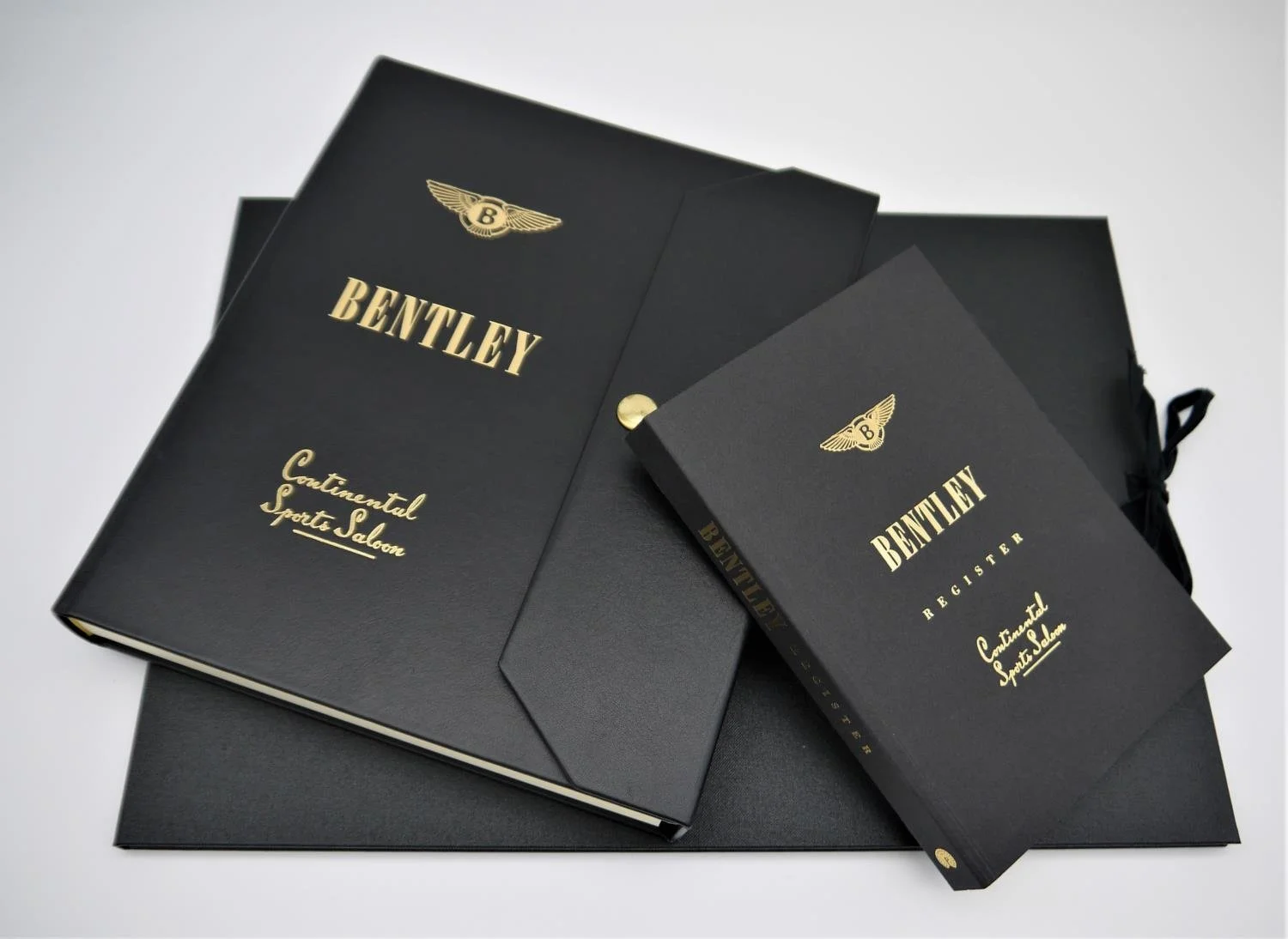 Black Bentley booklets labeled 'Contimental Sports Saloon' and 'Register' with gold embossed text and logos, placed on a black folder.