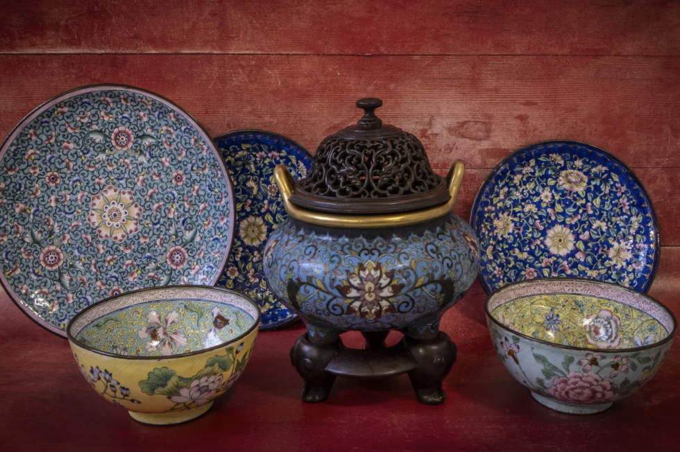 Decorative Asian-style ceramics, including bowls and plates with floral patterns, arranged on a red wooden surface.