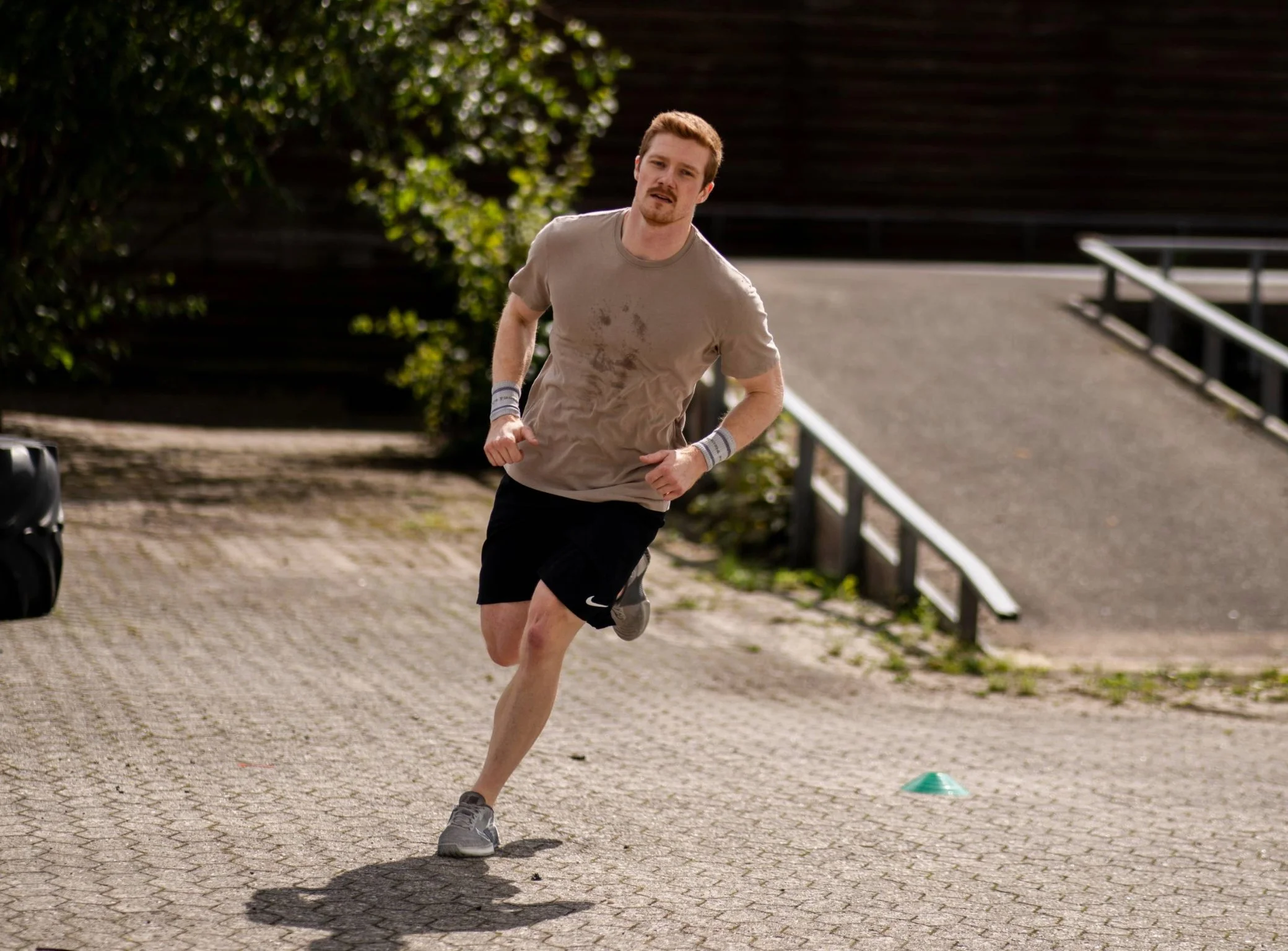 En mand løber udendørs, iført sportstøj og løbesko, på en asfaltsti med en grøn kegle foran sig.