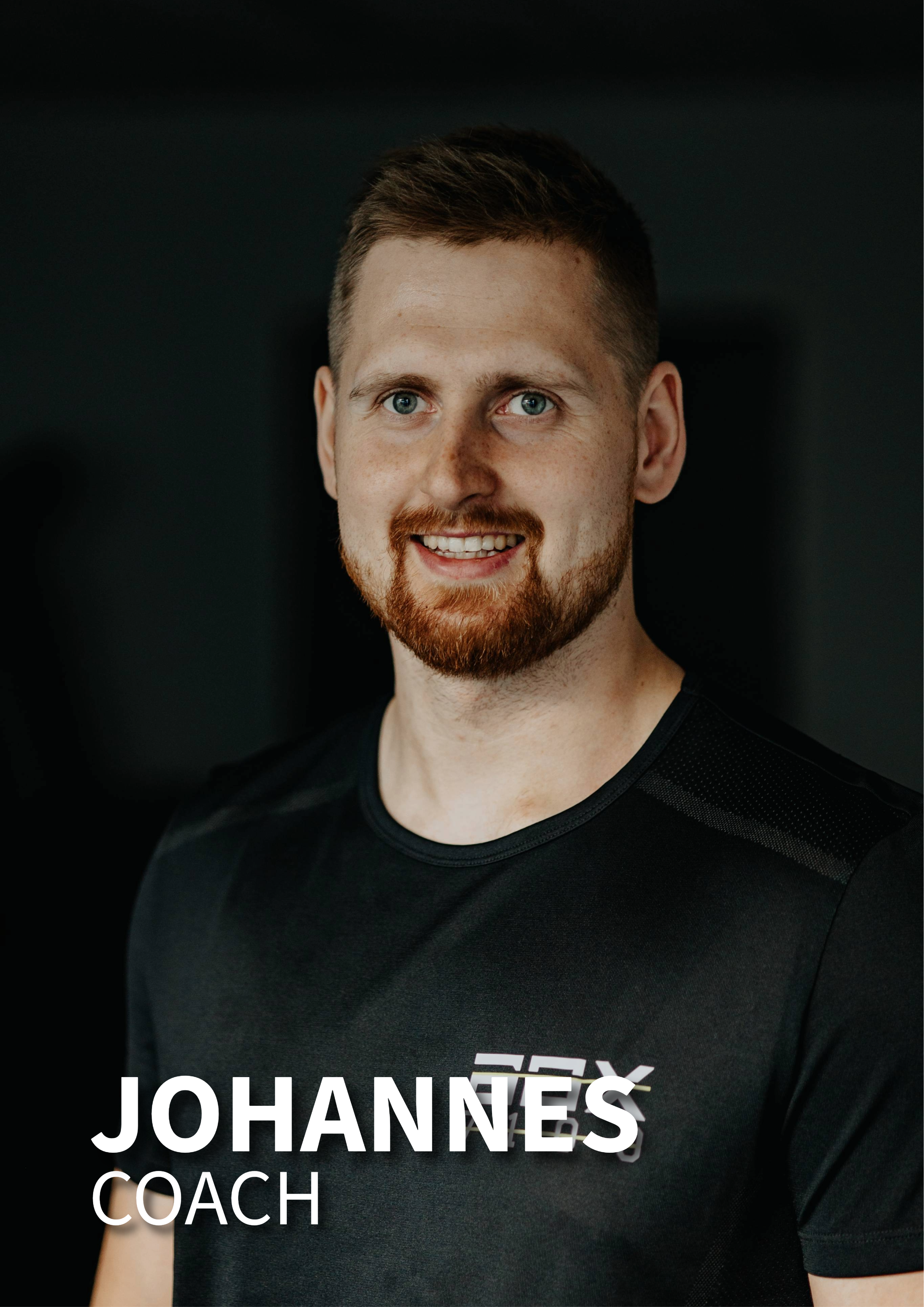 Portræt af en mand med lysebrunt hår og skæg, iført sort træningstøj, mod en mørk baggrund.