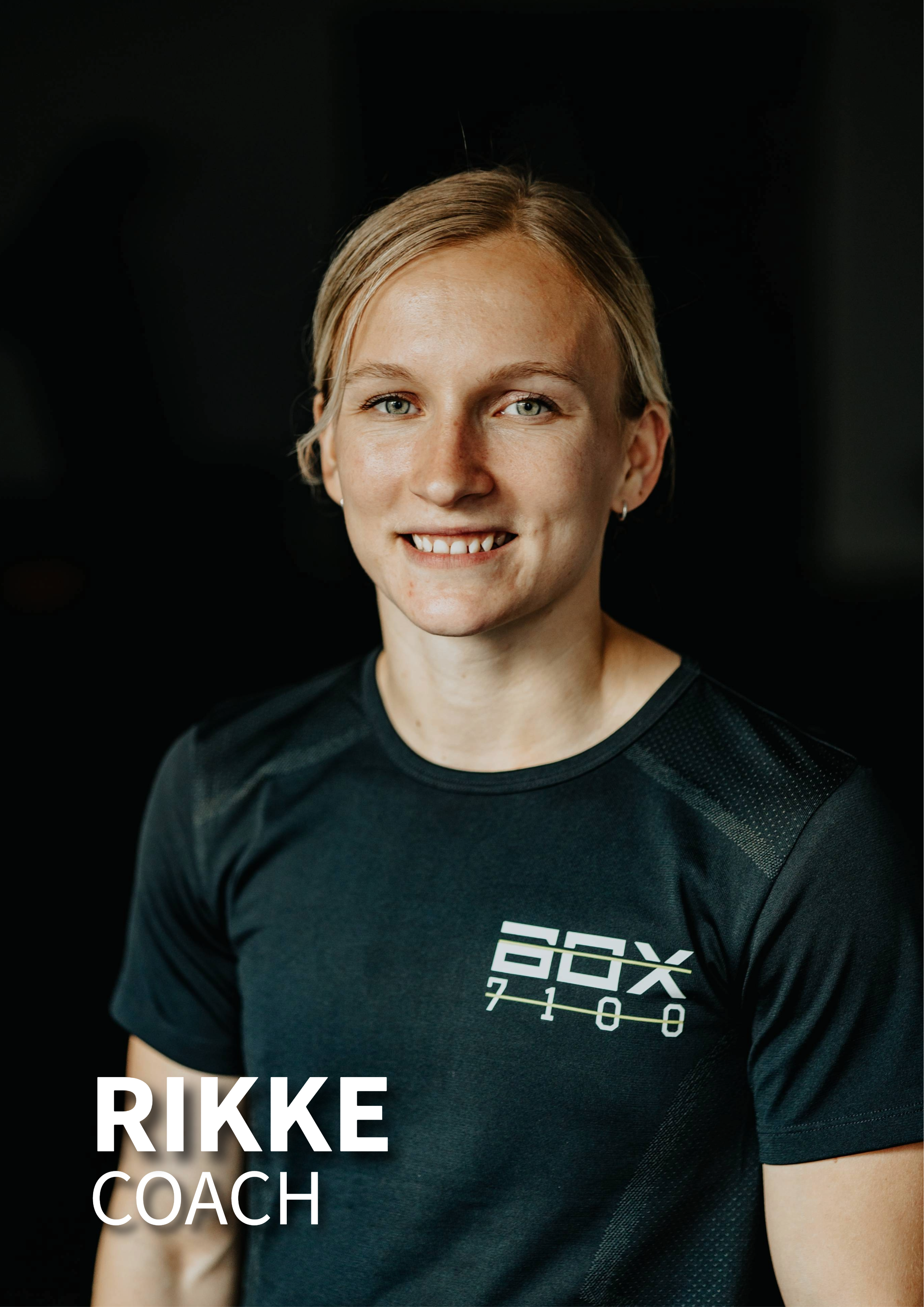 Portræt af en blond kvinde iført sort trænings T-shirt med teksten 'FOXX 7100', smilende mod kameraet mod en sort baggrund.