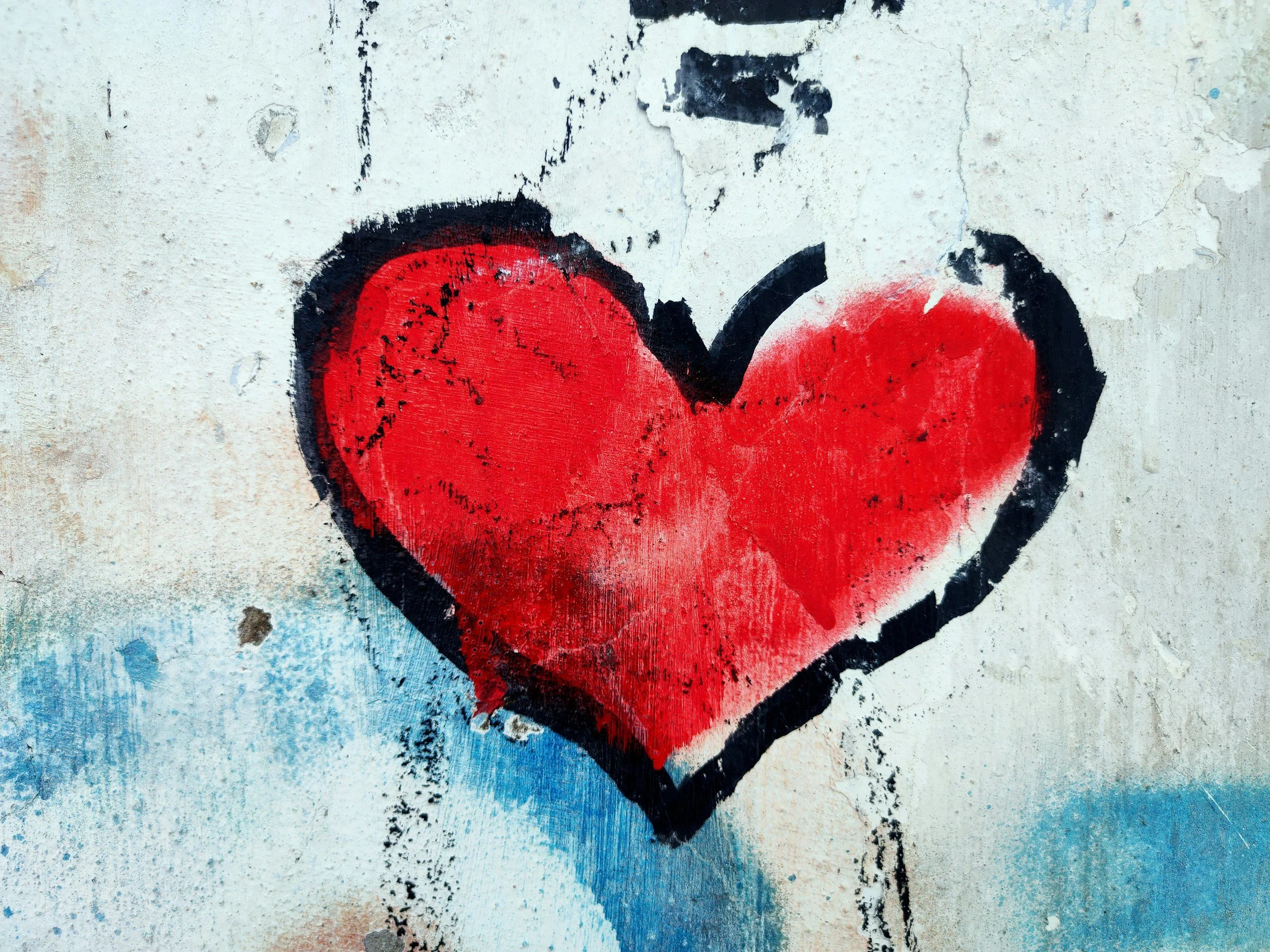 Graffiti of a large red heart with black outline on a textured wall.