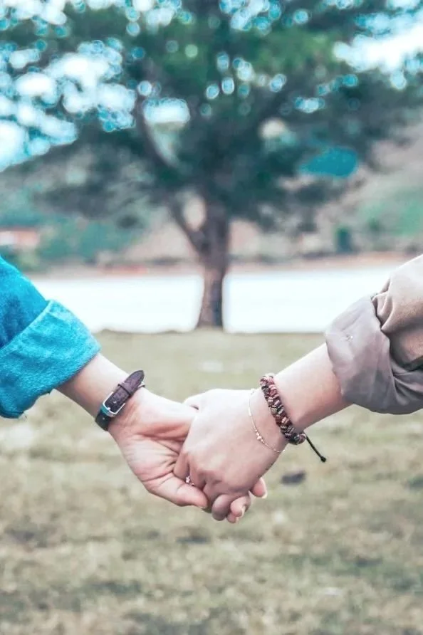 Couple holding hands outdoors by a lake, symbolizing connection, trust, and relationship growth.