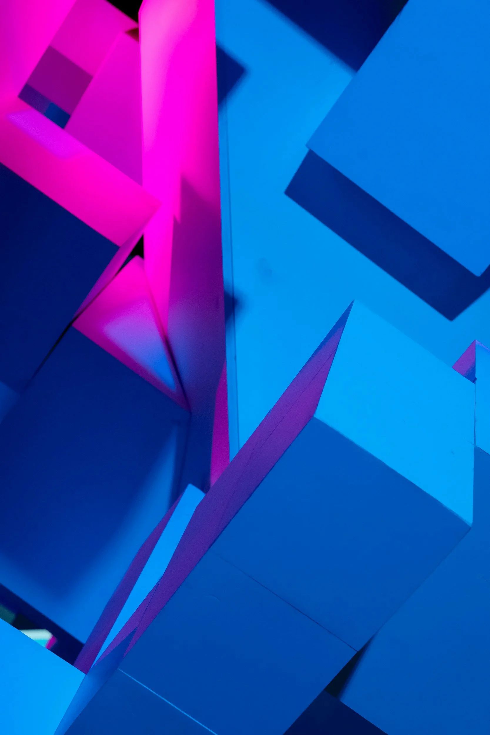 Abstract geometric installation with sharp-edged panels illuminated in pink and blue lighting.