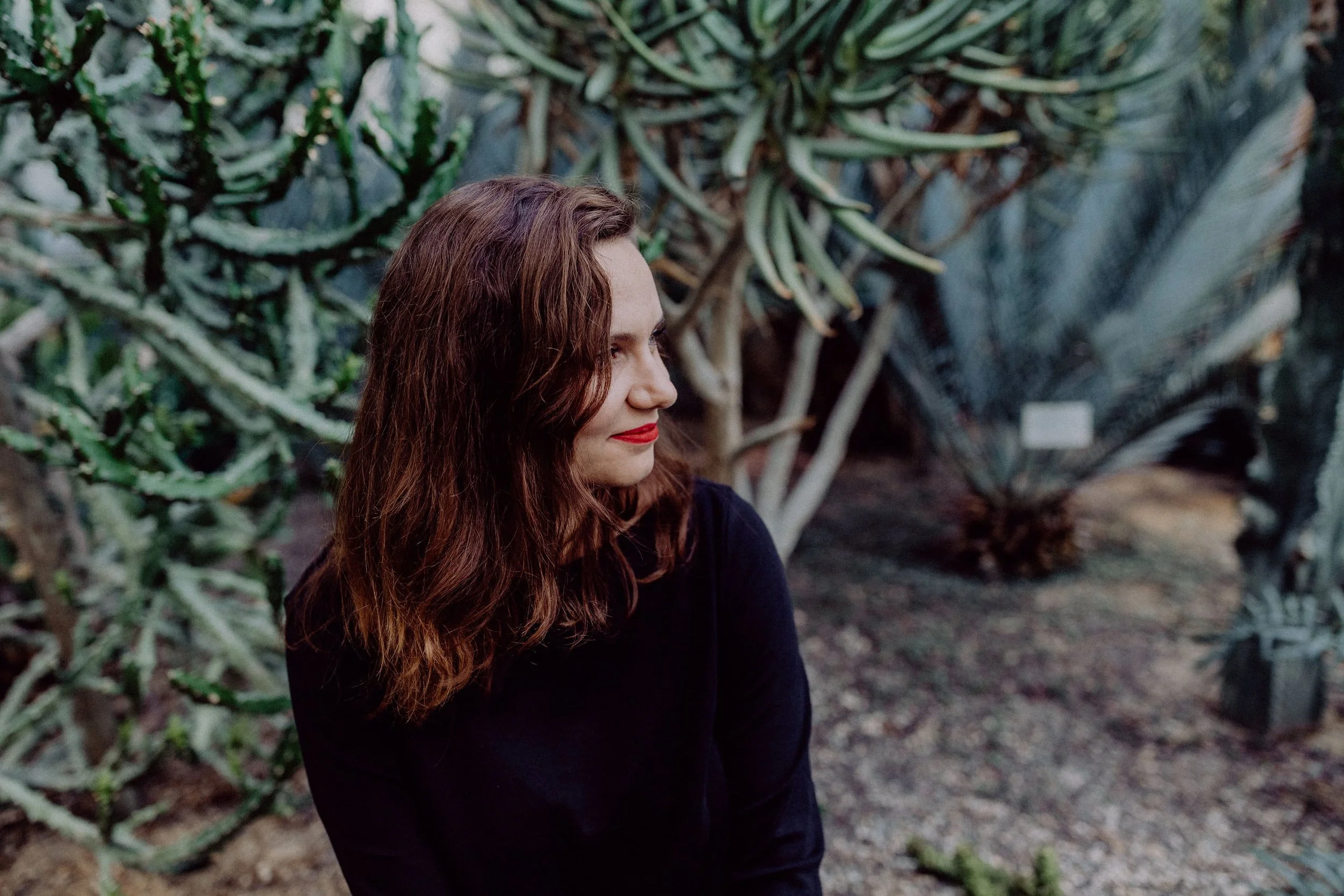 Alexandra Polunin sitzt vor einer grünen Pflanze und schaut zur Seite