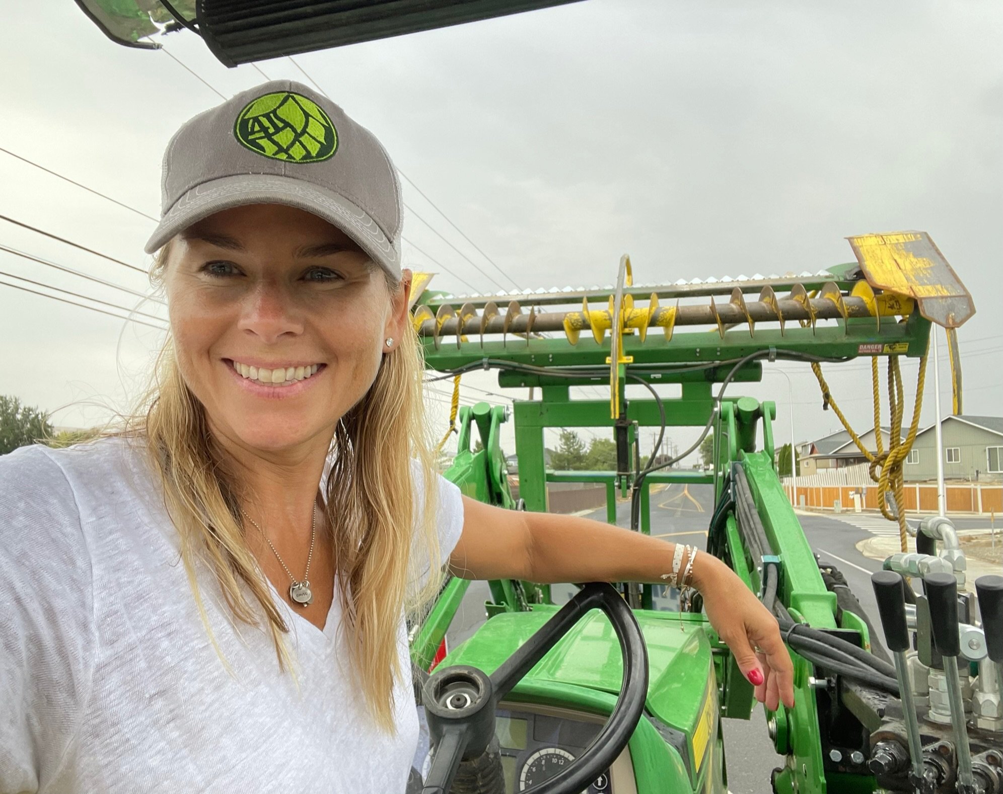Woman smiling in front of green tractor on a cloudy street with houses and power lines.
