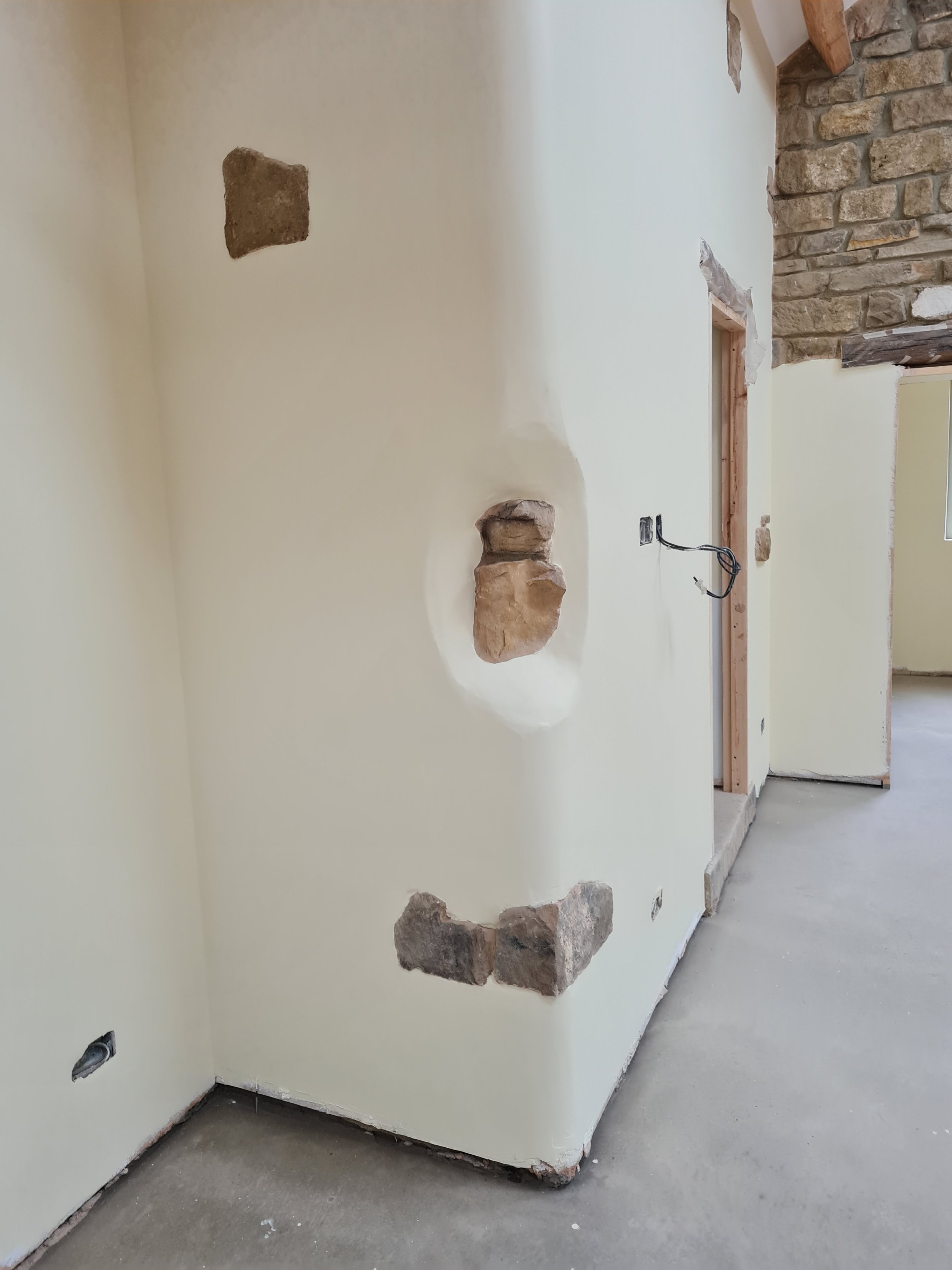 A room under construction with exposed bricks and electrical wiring, partially covered with drywall.