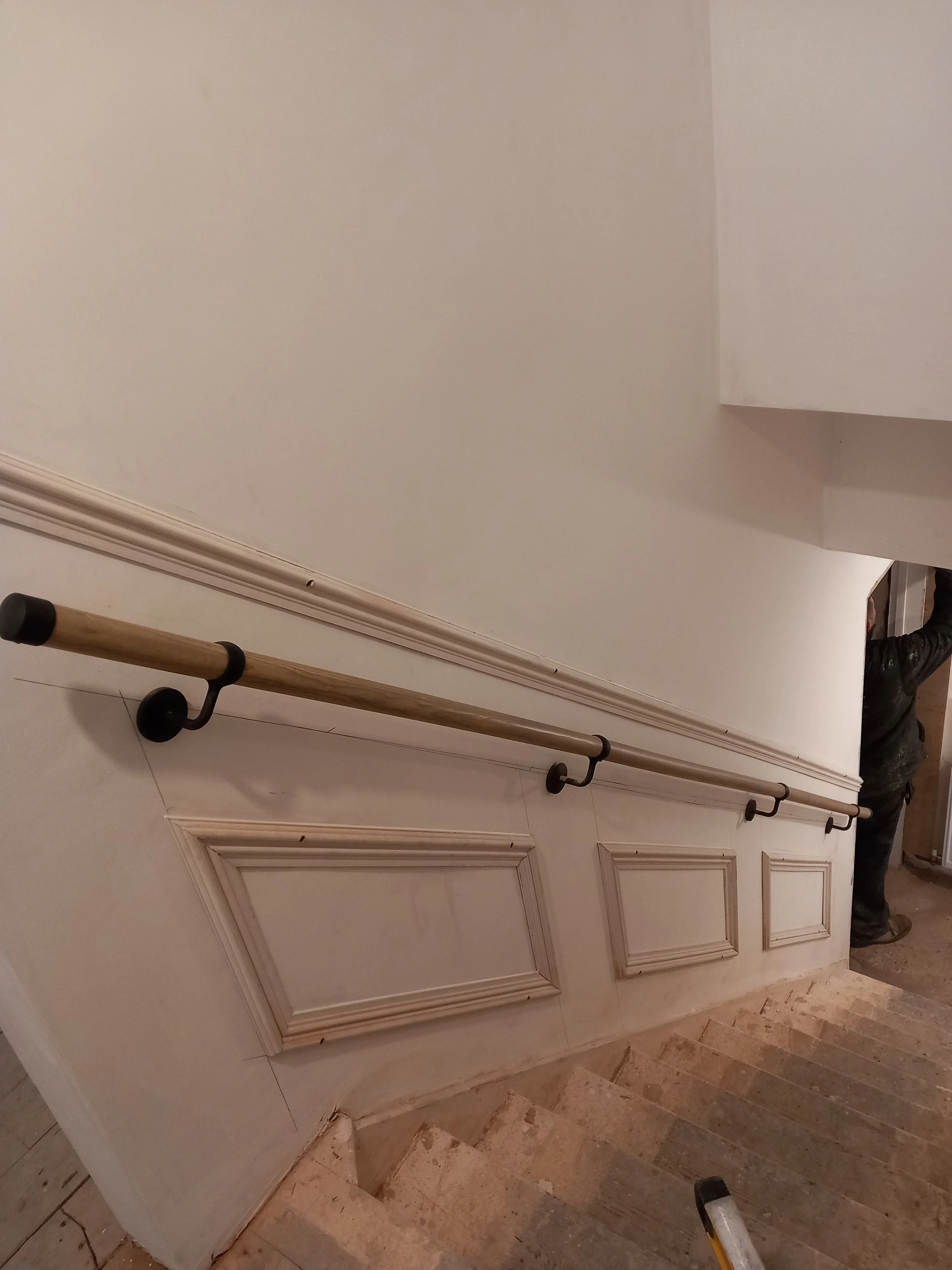 Wooden handrail mounted on a partially paneled staircase wall in a home under renovation.