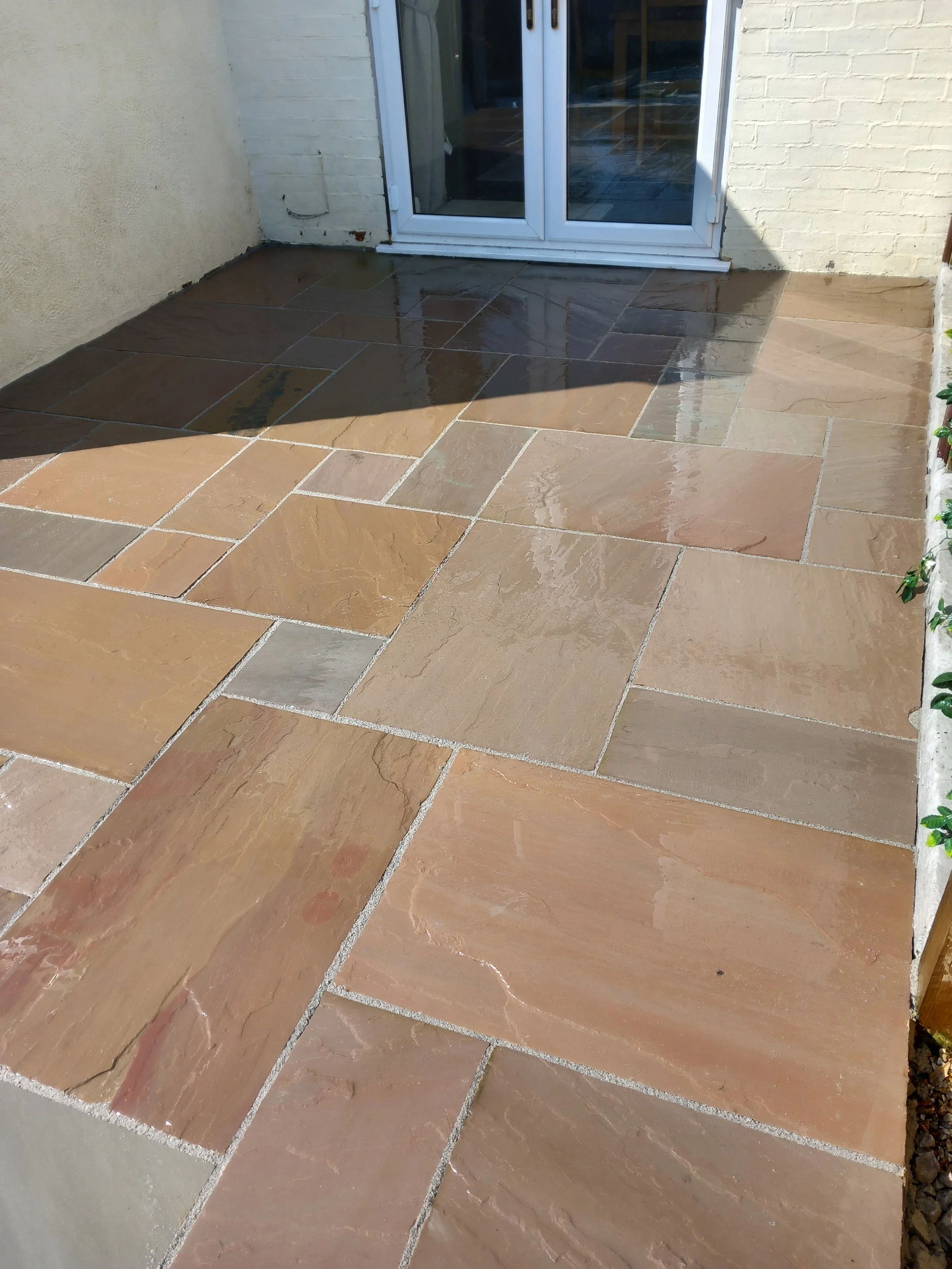 Wet stone patio outside a glass door, with water reflecting on the surface.