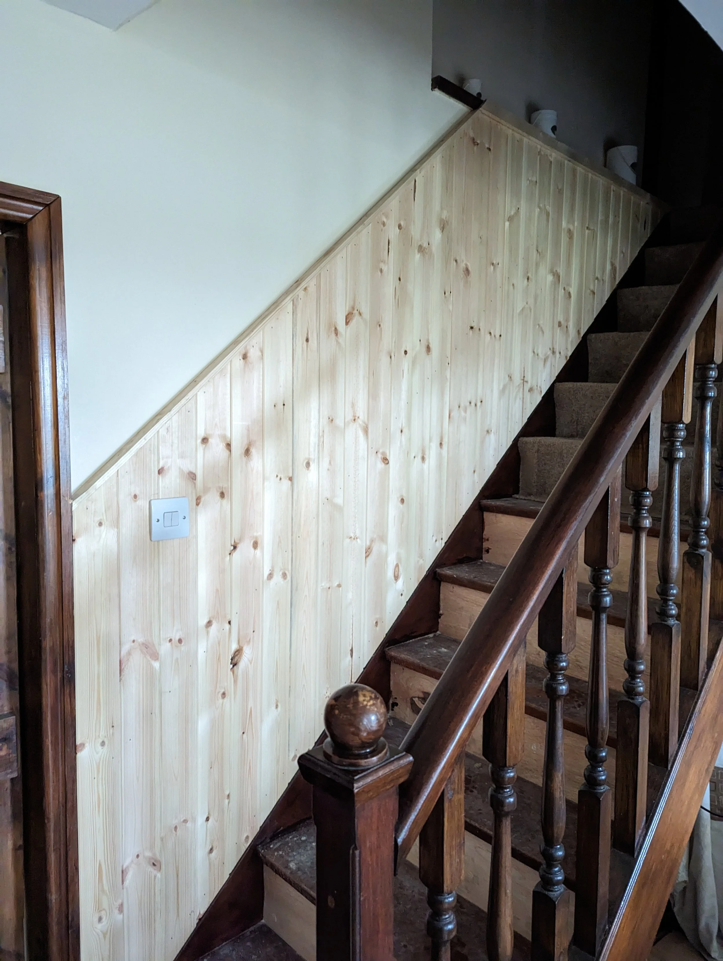 Wood-paneled wall beside a staircase with dark wooden banister and carpeted steps.