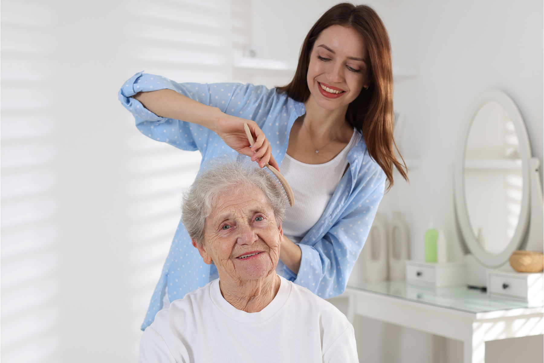 Elderly woman receiving assistance with personal hygeine and grooming. Support worker is brushing the hair for the participant the bathroom
