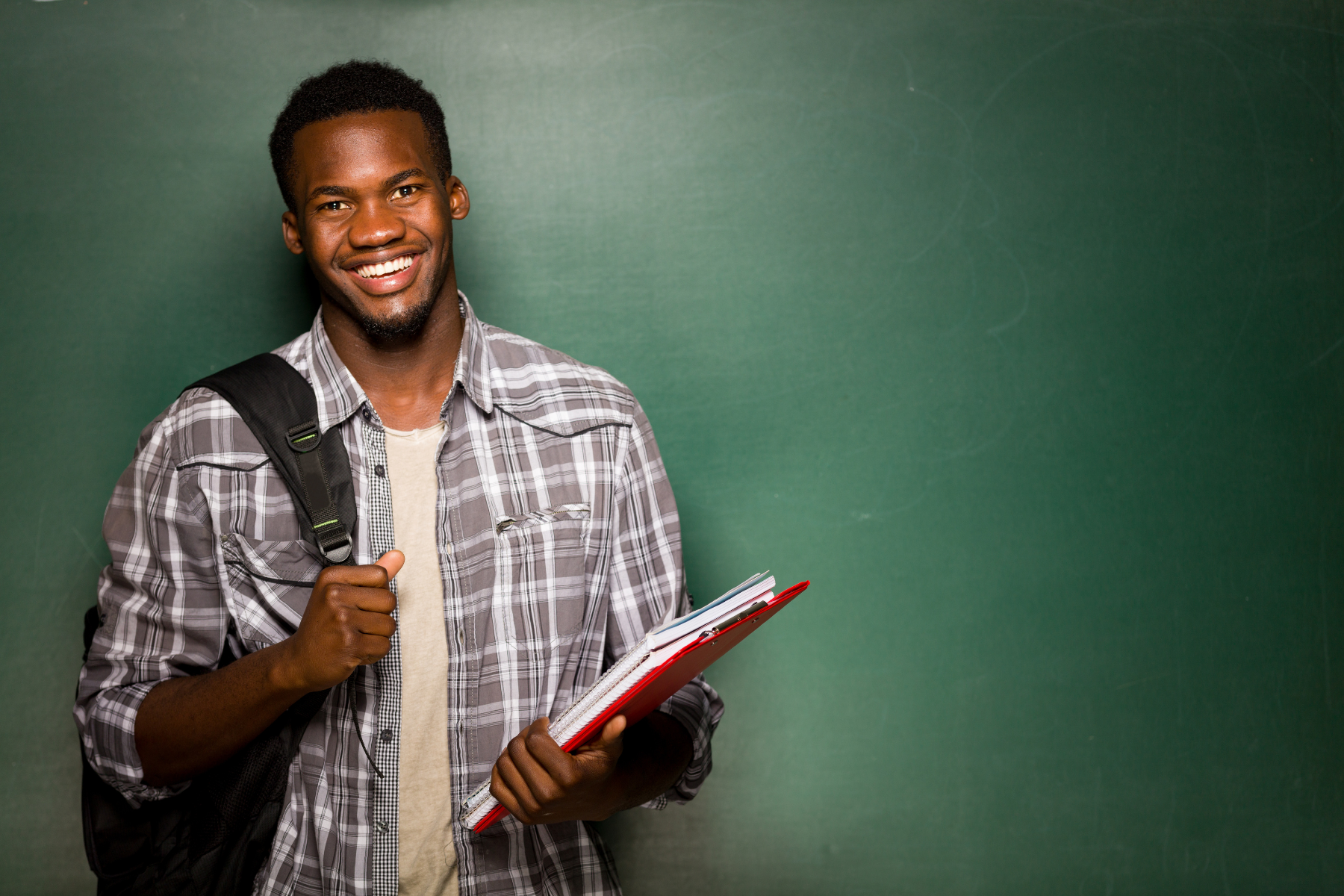 Student standing infront of a blank wall holding a book ready to learn