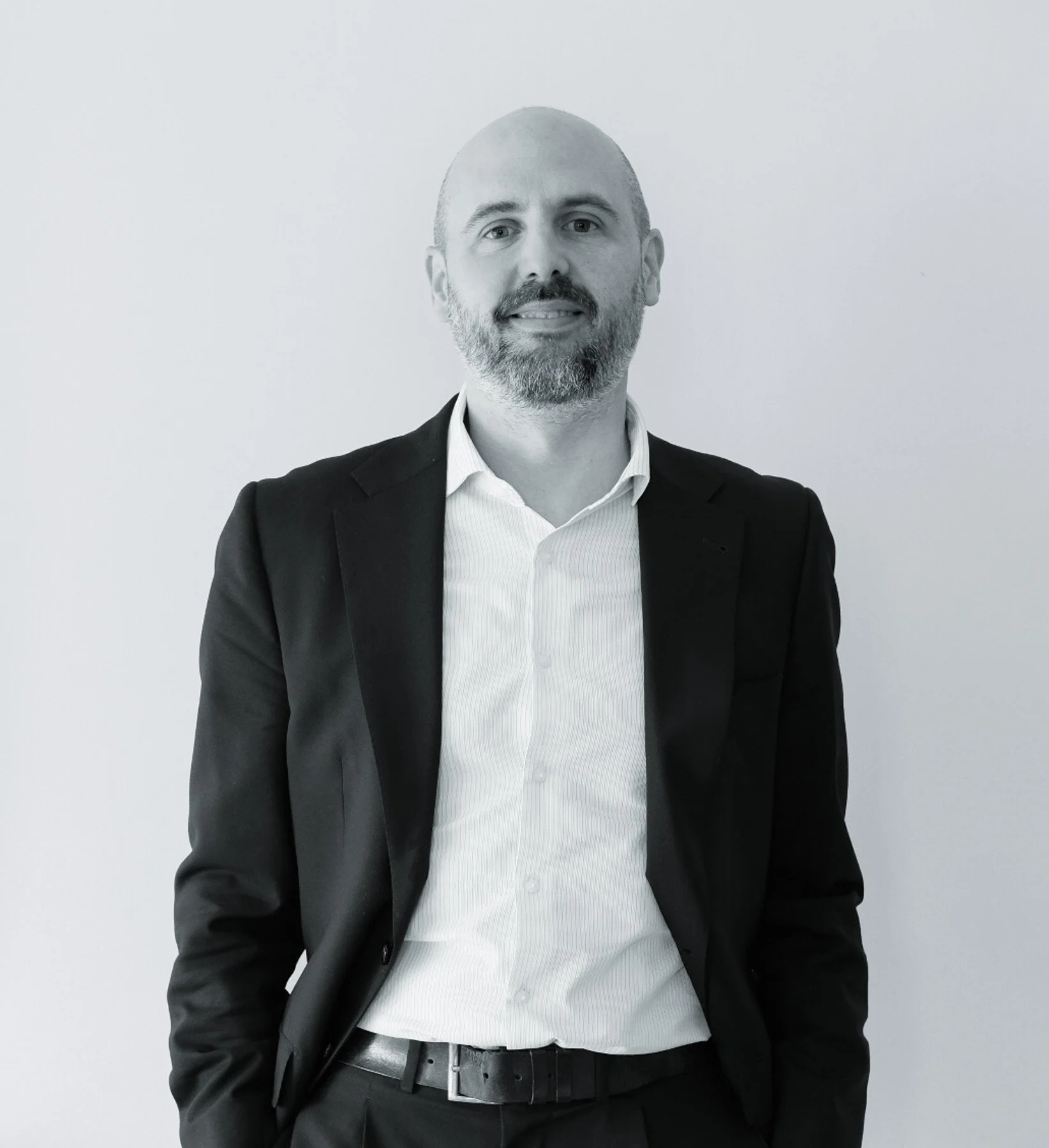 David del Valle, abogado. Vestido con saco negro y camisa blanca, de cabello corto y barba, de pie frente a pared blanca.