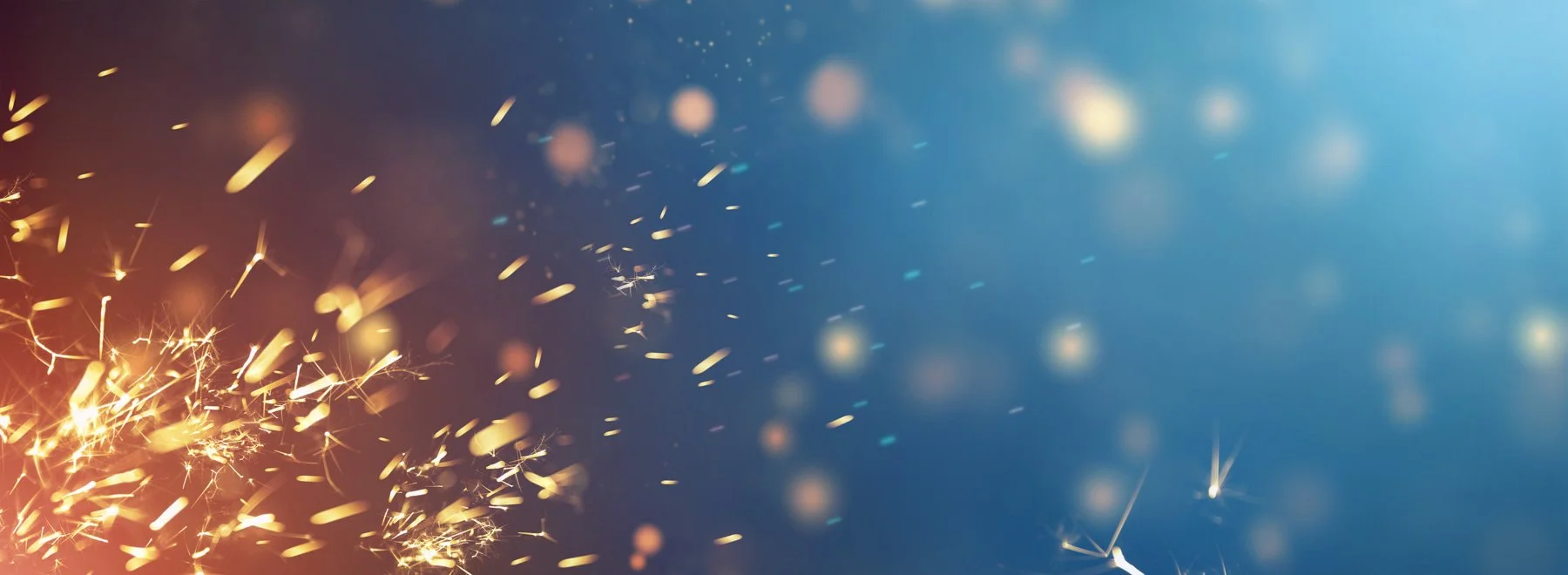 Chispas doradas y blancas volando en un fondo difuso azul y oscuro.