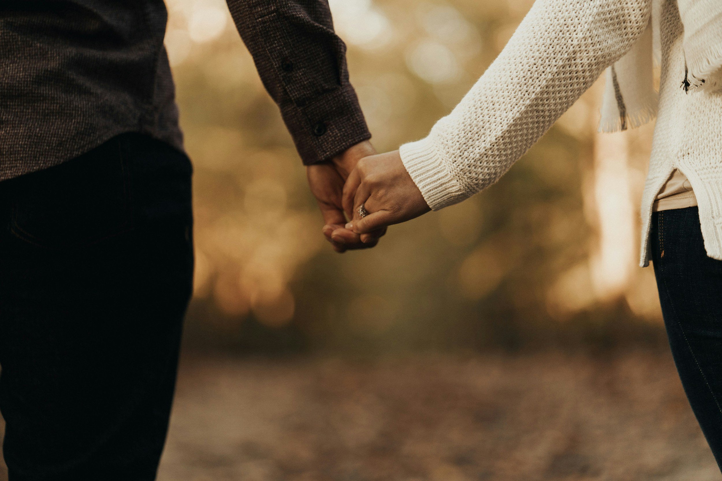Two people holding hands, one wearing a dark plaid shirt and the other wearing a cream-colored cardigan.