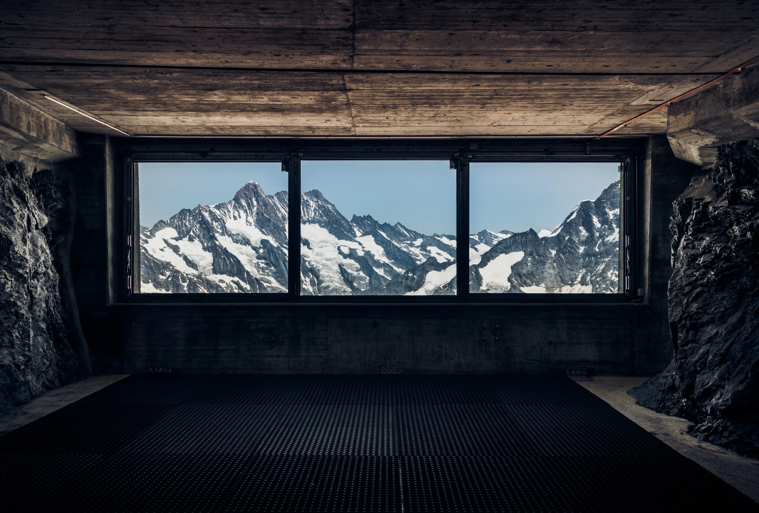 Mountain range with snow-covered peaks seen through large indoor window.