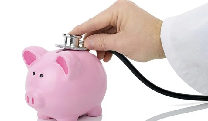 Person's hand using a stethoscope on a pink piggy bank.