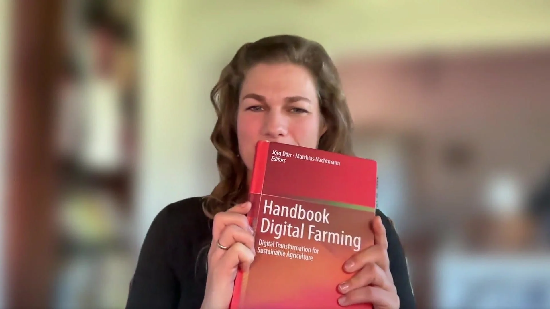 Catharina van Delden holds up the Handbook Digital Farming during the webcast recording with Matthias Nachtmann