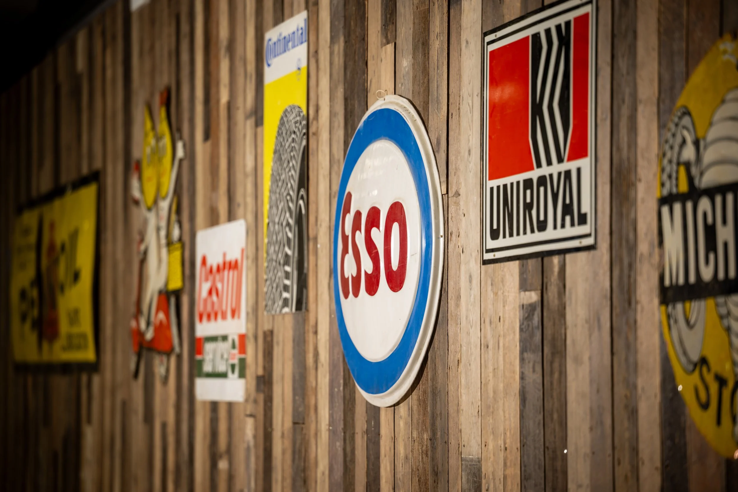 Collection of vintage signs on wooden wall, including a red, white, and blue 'SOS' sign and various other retro signs.