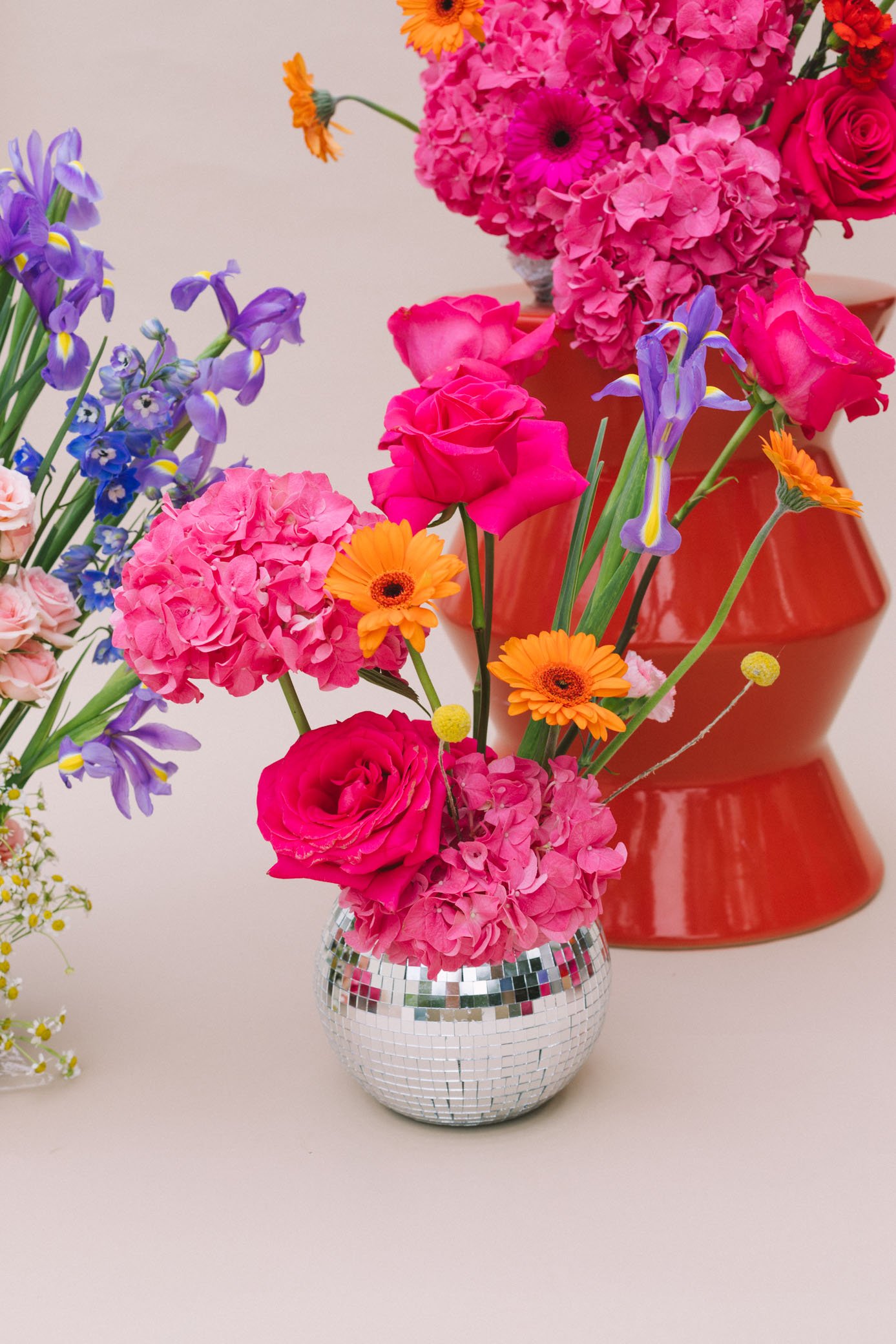 Vase de fleurs avec des roses roses, des hortensias roses, des iris violets, des marguerites orange et autres fleurs dans un décor minimaliste.