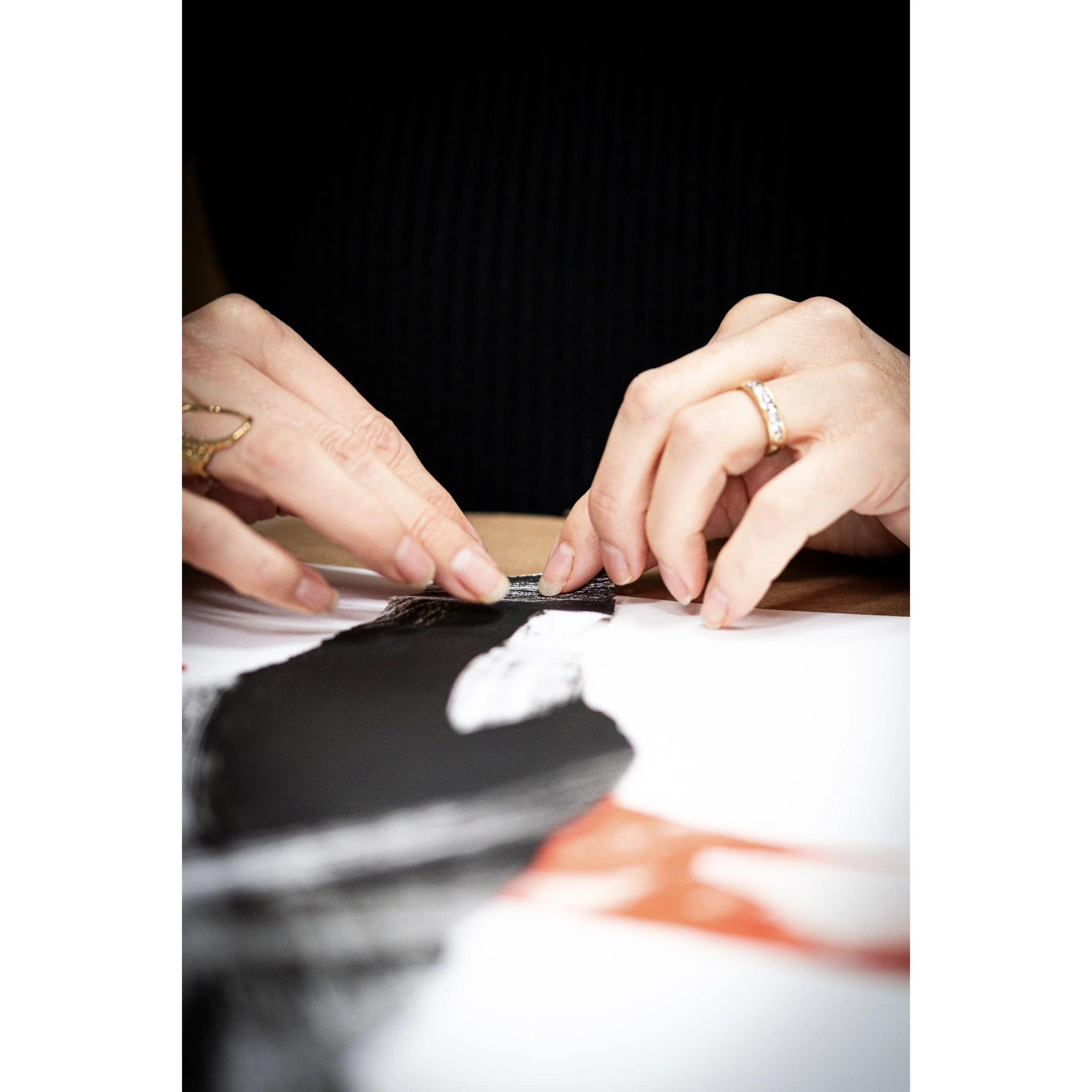 Mains d 'une personne créant un collage avec des papiers et des tissus avec des anneaux aux doigts.