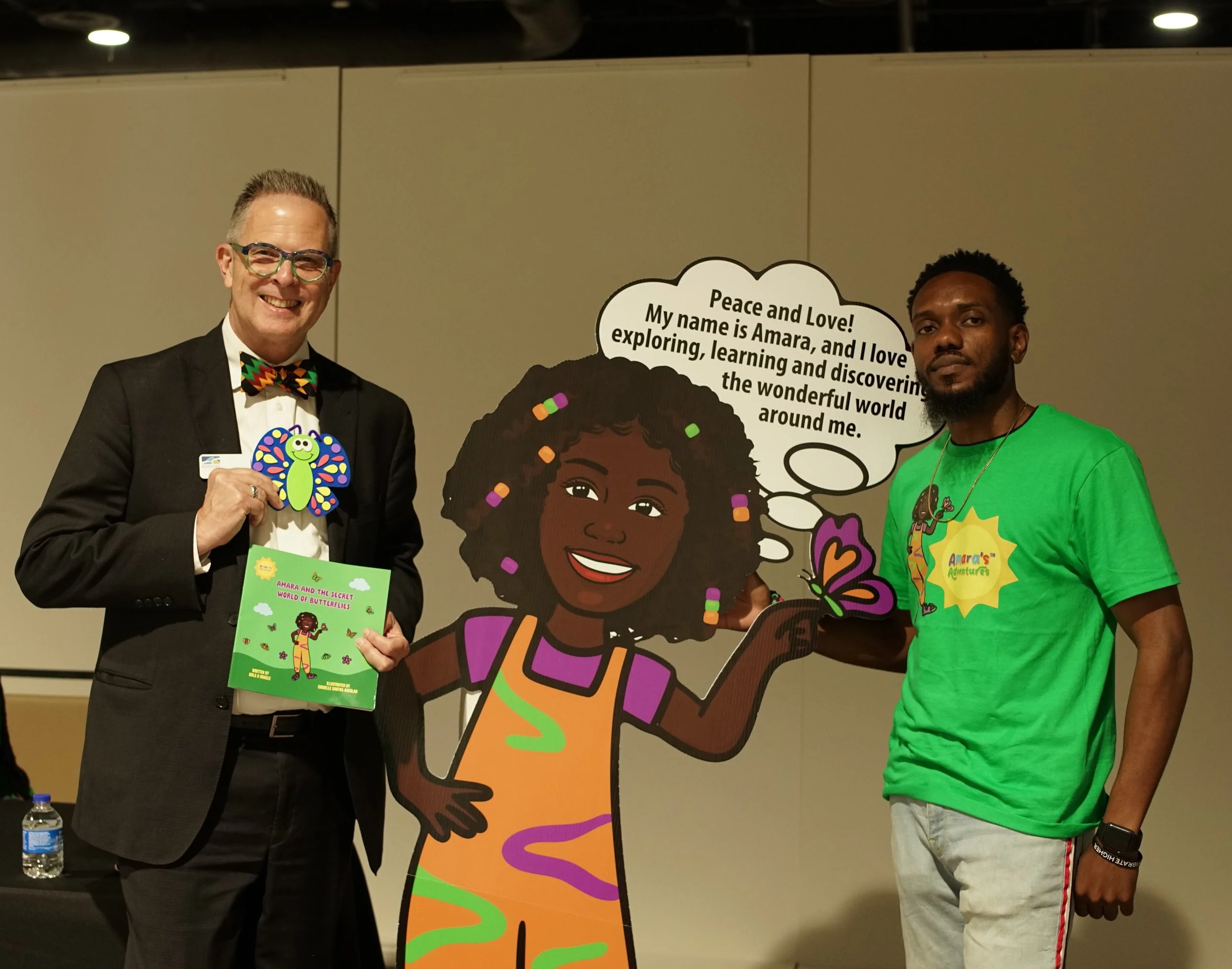 Roanoke Mayor Joe Cobb holds Amara and the Secret World of Butterflies beside an Amara character standee and Sage Love