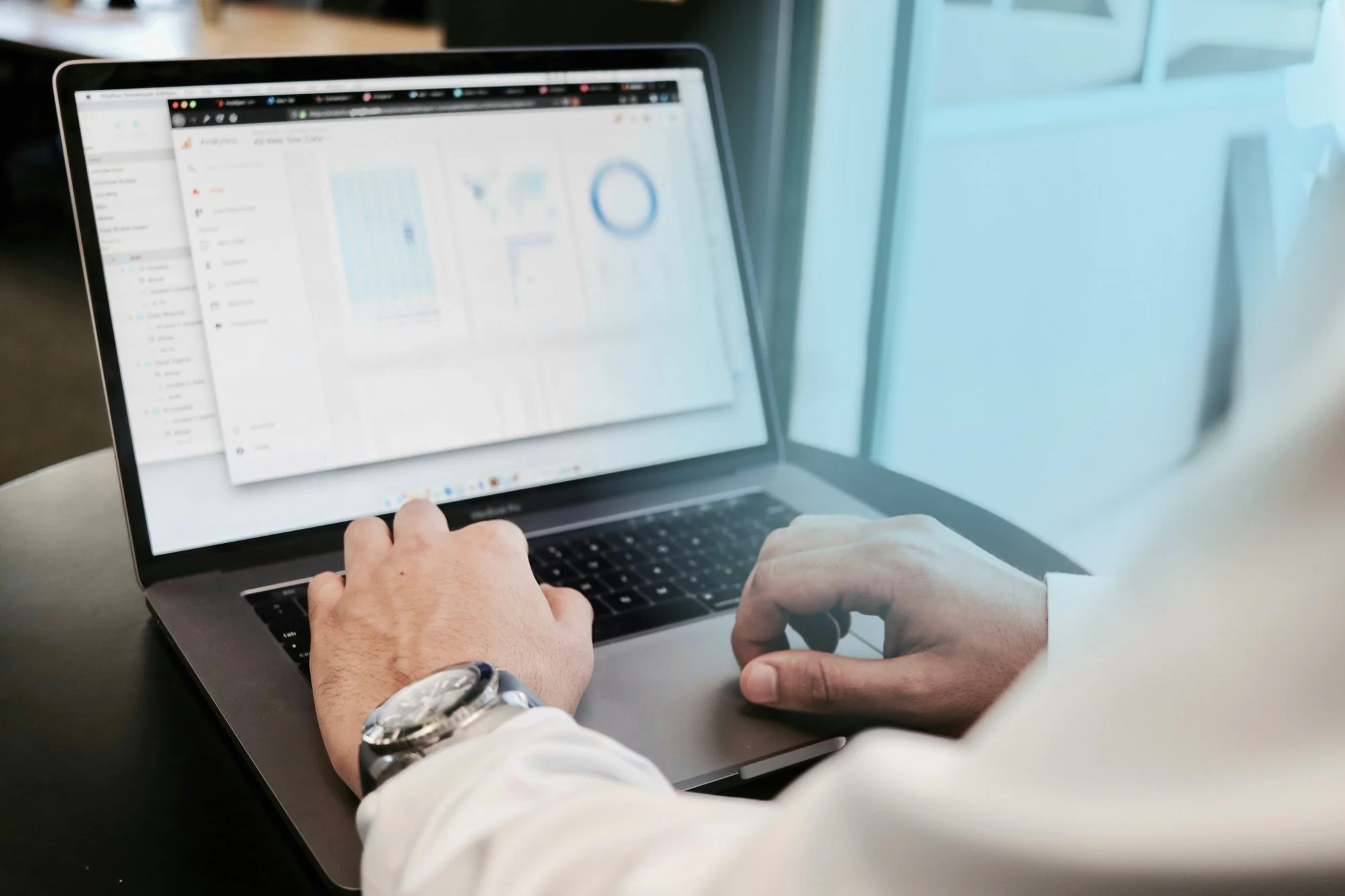 A person using a laptop at a desk, with a blurred digital chart or dashboard displayed on the screen.