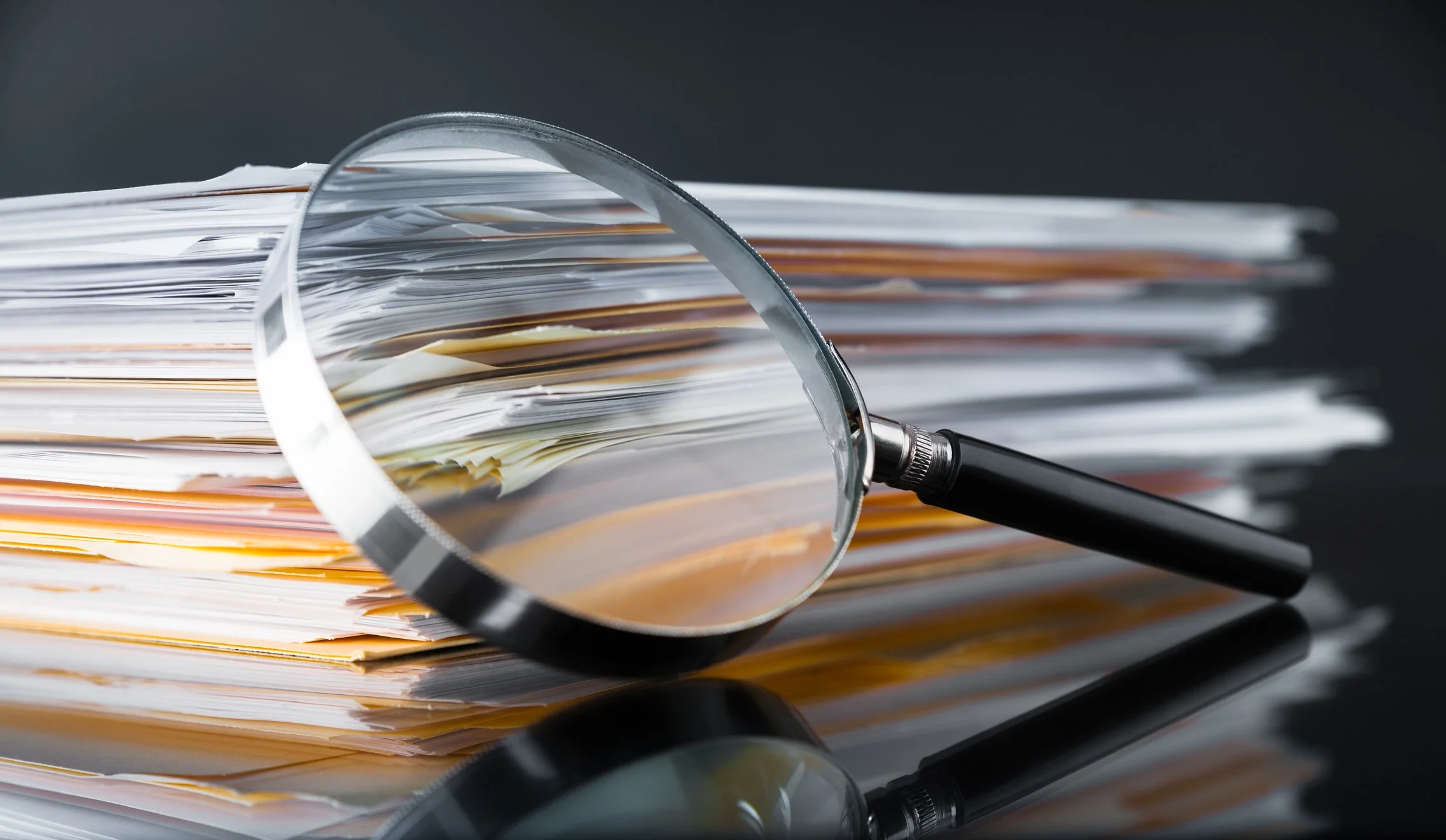 A magnifying glass placed over a stack of QMS documents signifying Quality Management System gap assessment.
