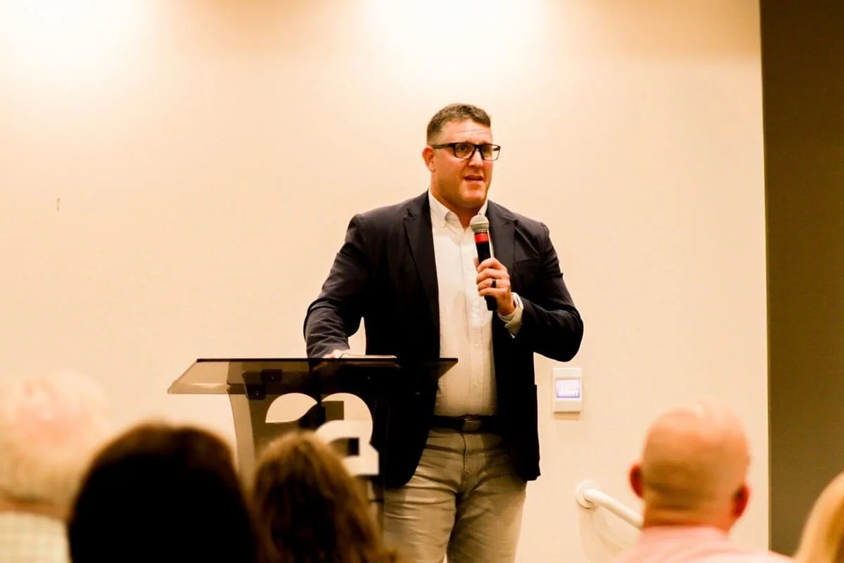 Man in glasses and suit speaking at a charity event to support youth ministry.
