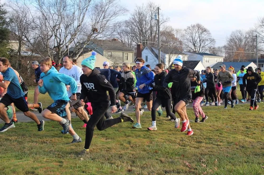 Group of runners starting a race on a grassy field on a cool day.