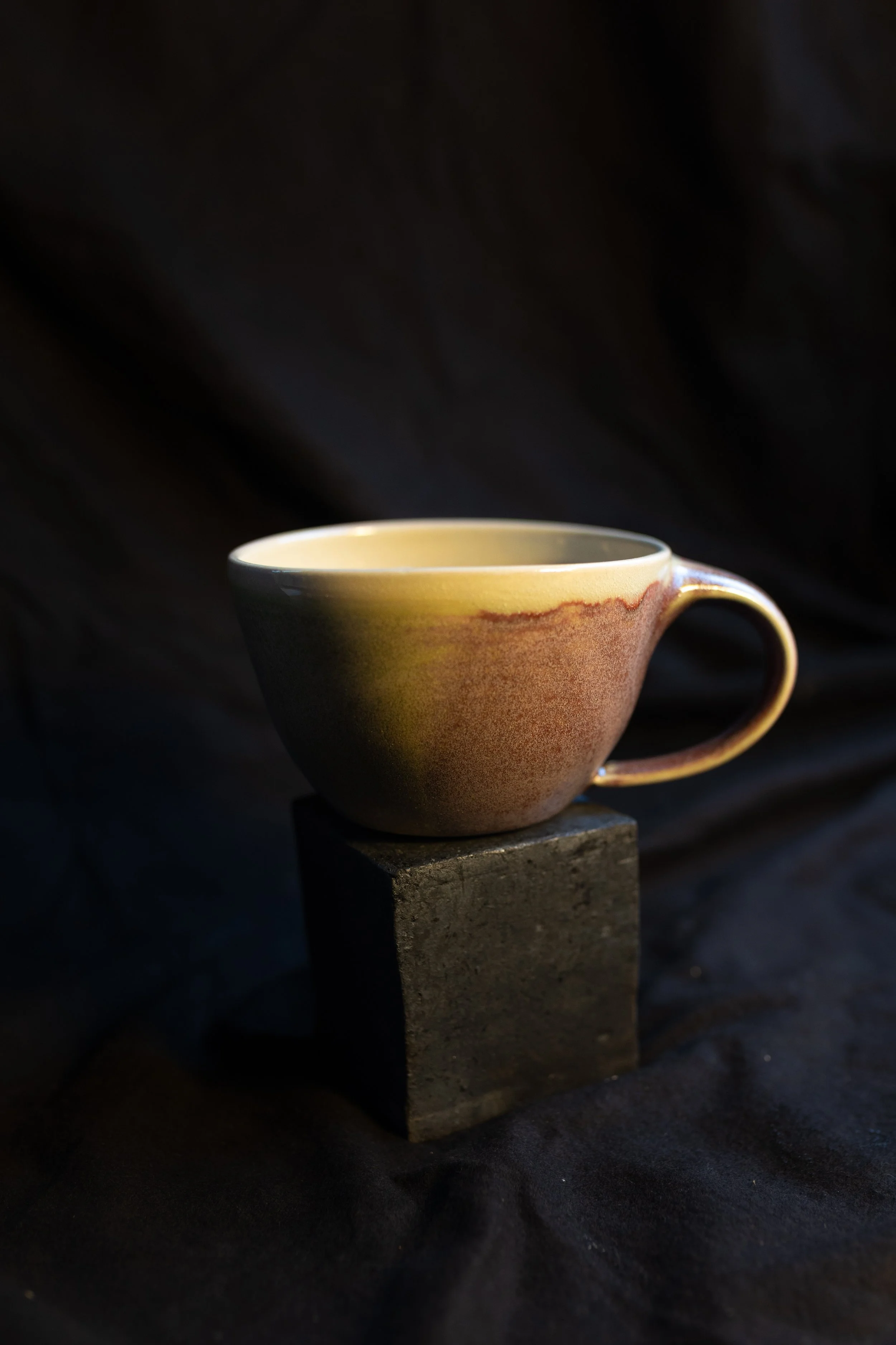 Eine Teetasse auf einem schwarzen Block, dunkler Hintergrund, minimalistische Beleuchtung.