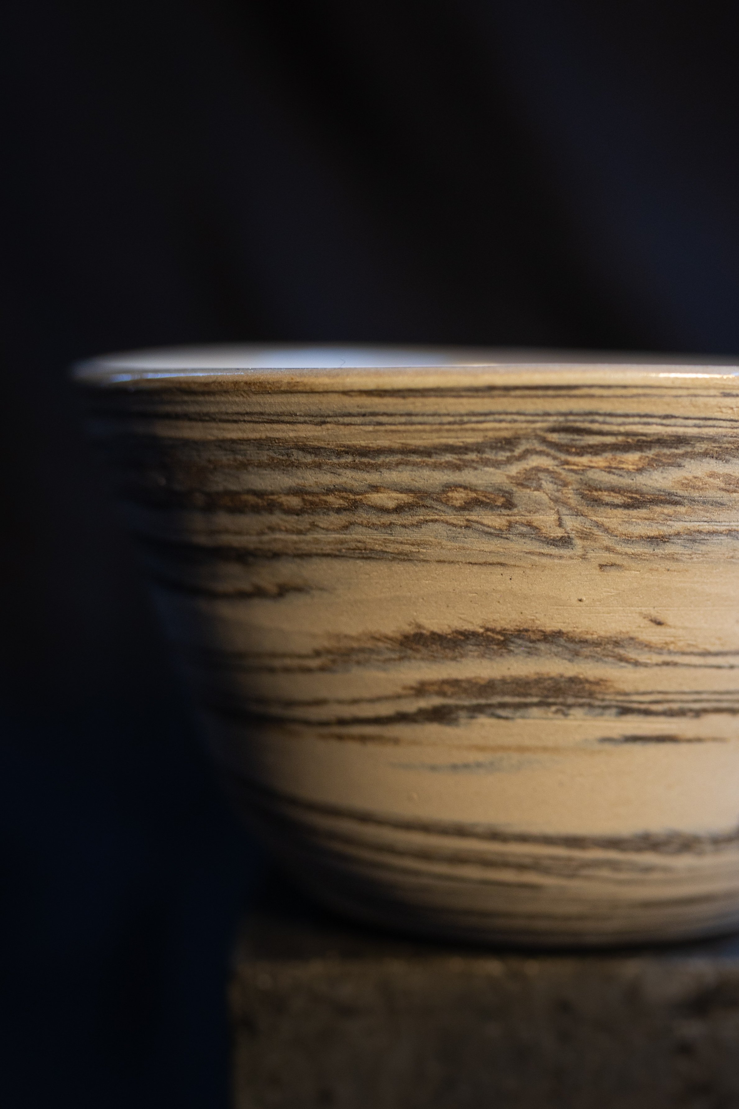 Nahaufnahme einer Schale aus Holz mit sichtbarer Maserung auf einer dunklen Oberfläche.