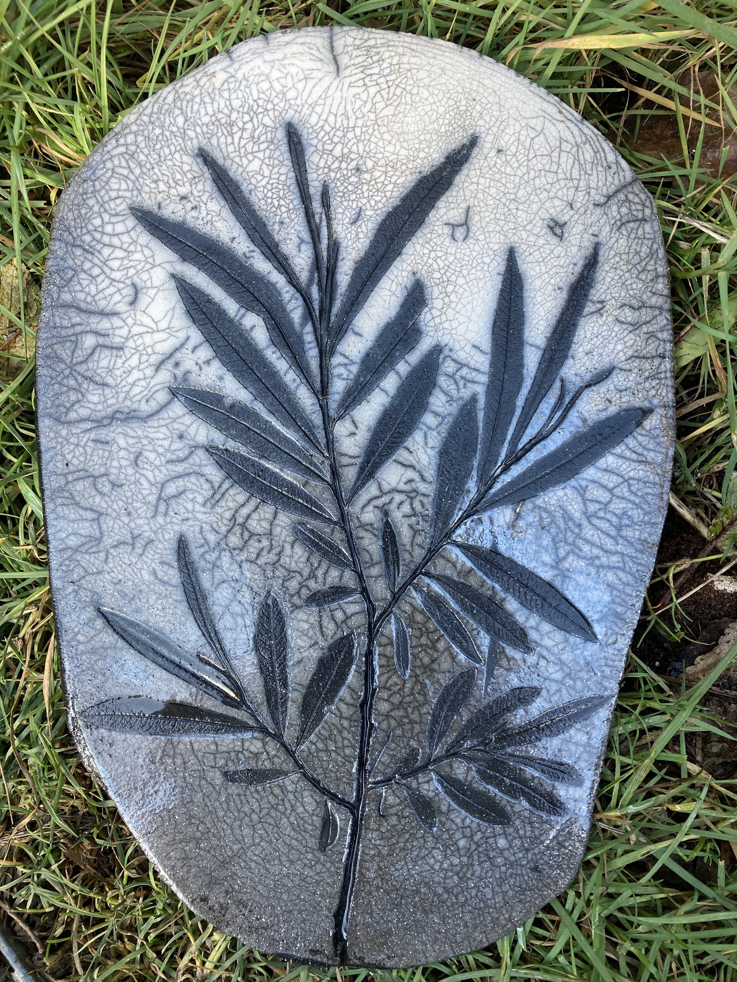 Eine Keramik-Kachel mit Raku von Baumzweig mit Blättern im Gras.