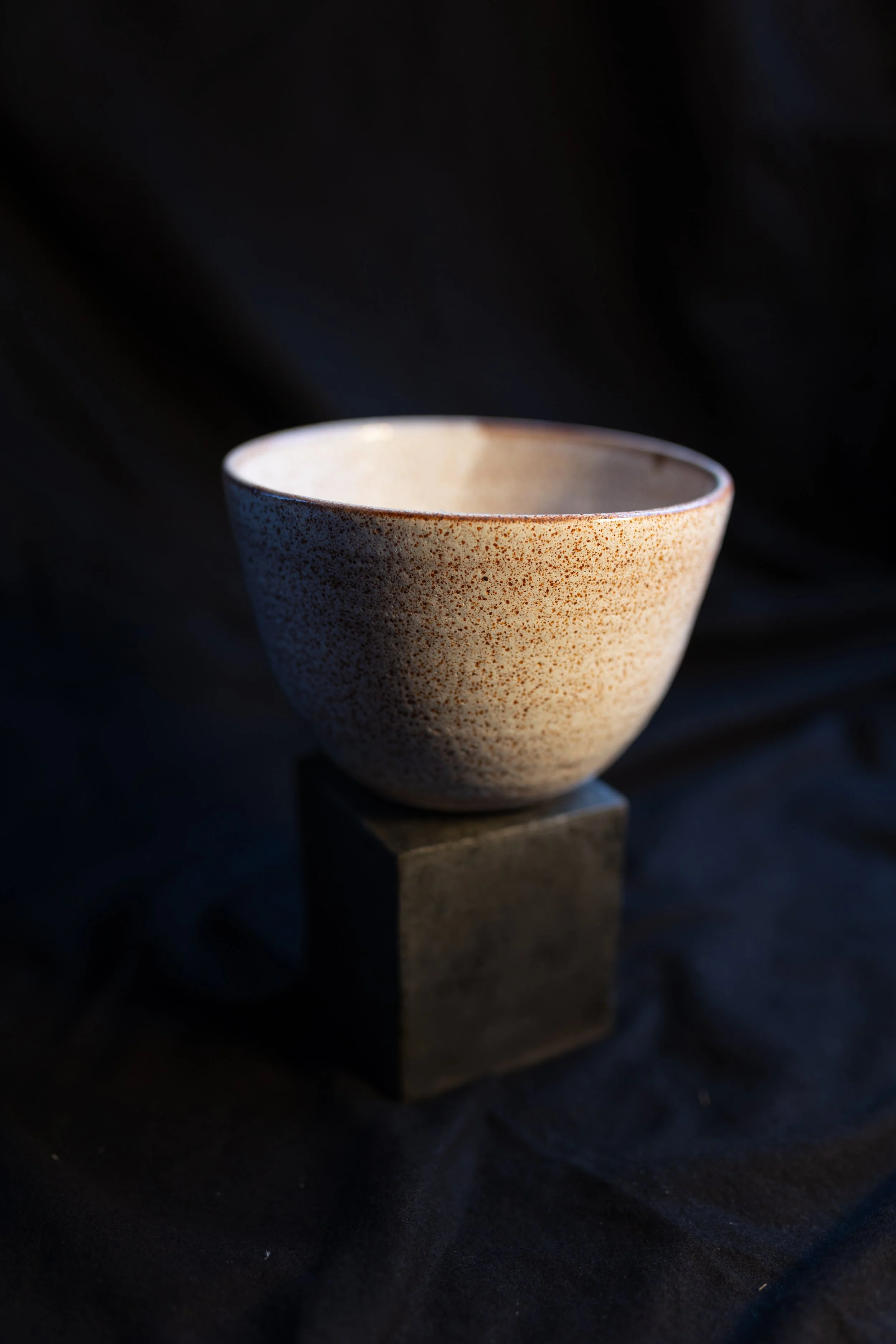 Keramik-Schüssel auf einem kleinen schwarzen Würfel mit dunklem Hintergrund, Beleuchtung hebt die Textur hervor.