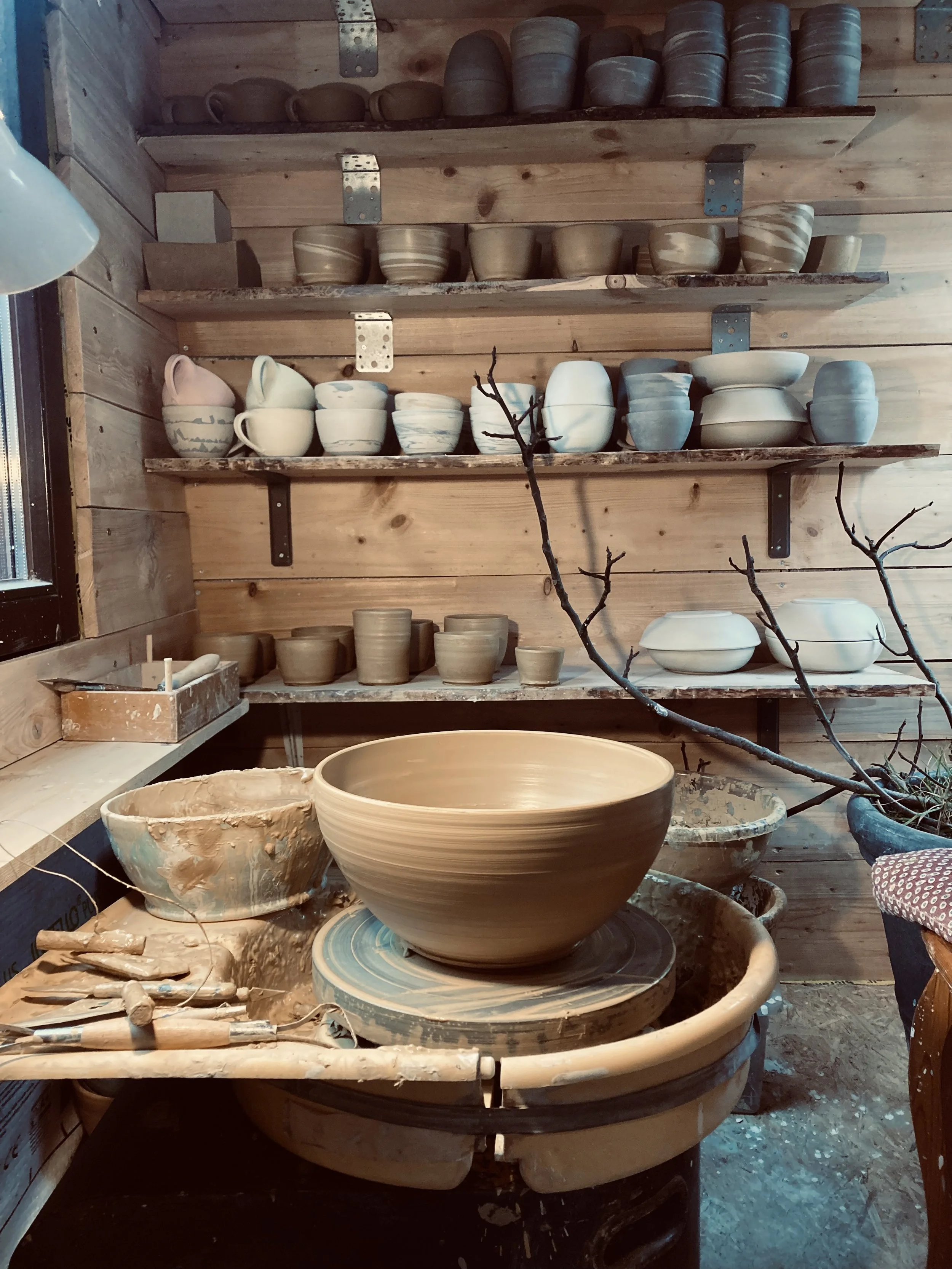 Keramikatelier mit verschiedenen keramischen Schalen und Töpfen auf Regalen und an der Töpferscheibe